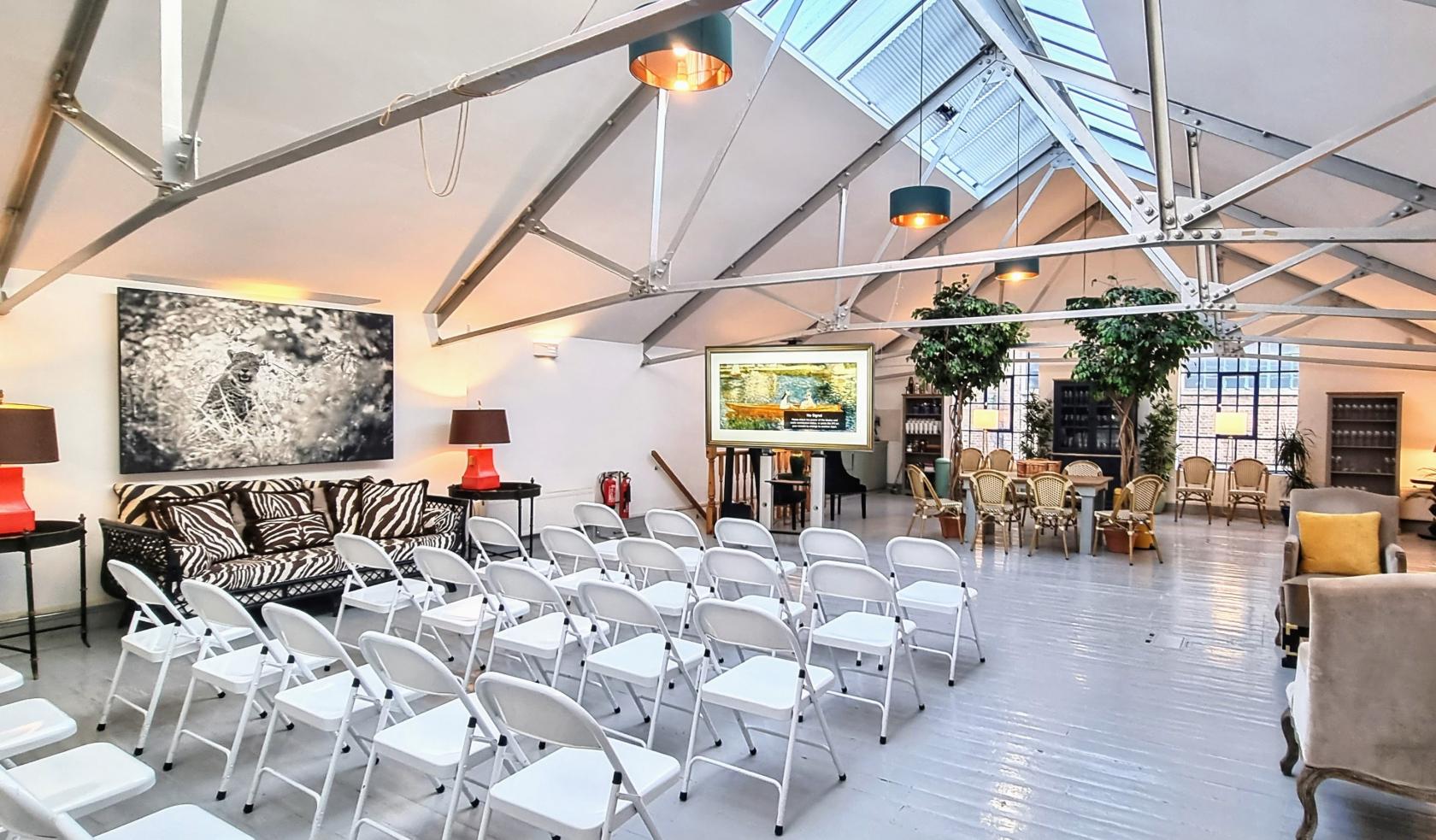 A photo studio with skylights, white folding chairs in rows, a zebra sofa, and indoor plants at L'Atelier Hoxton.