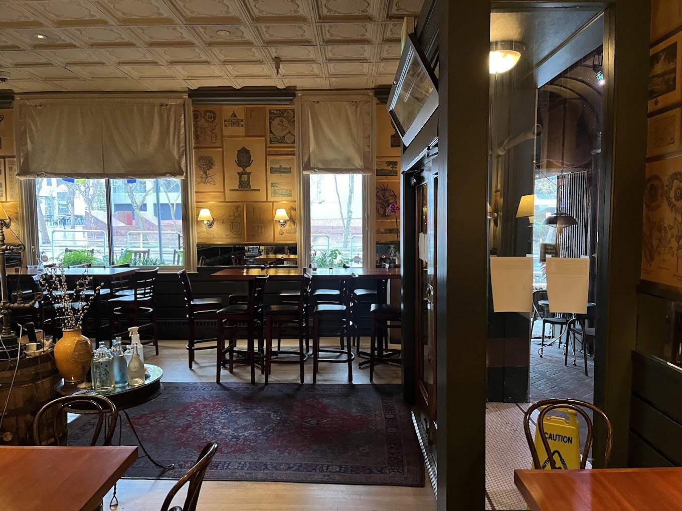 A restaurant with large windows, framed artwork on the walls, and communal tables with wooden chairs at The Fly Trap.