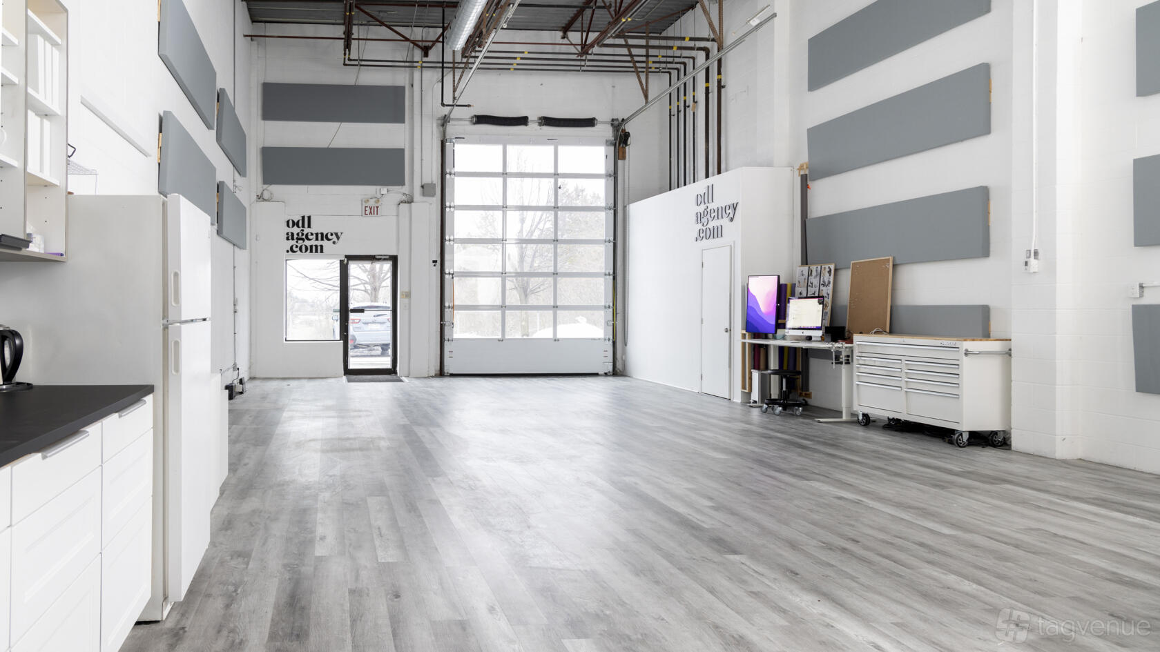 A photo studio with high ceilings, large roll-up windows, gray acoustic panels, and wood floors at ODL Studio.
