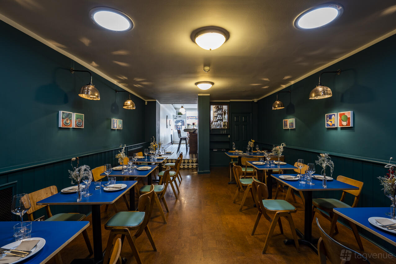 An event space in a restaurant with blue walls, round tables, and contemporary art at Klose & Soan.