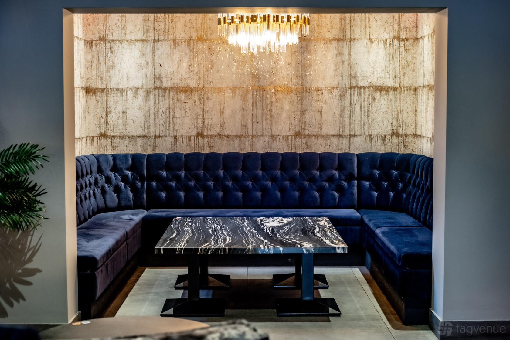 A lounge dining room with velvet tufted banquette seating and a marble table under a crystal chandelier at Fire & Ice Lounge Bar.
