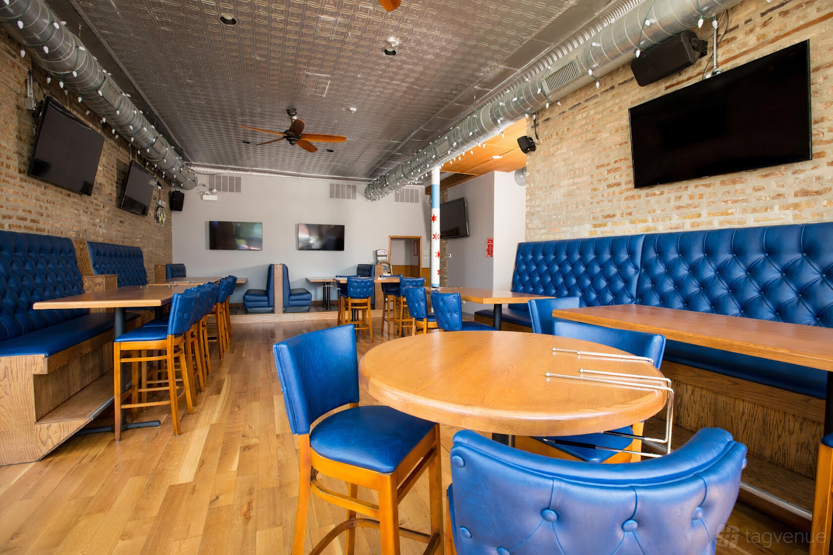 A restaurant with exposed brick walls, blue tufted banquettes, and wooden tables at Easy Street Pizza Chicago @ Portage Park.
