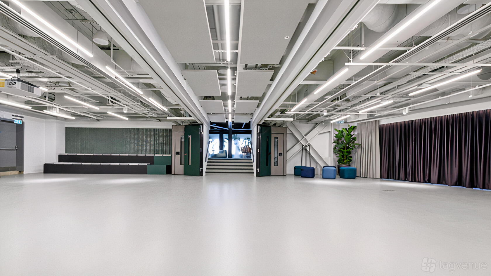 An event venue with exposed ceiling pipes, white floors, and a lounge area with blue seating at Storey Club Paddington.
