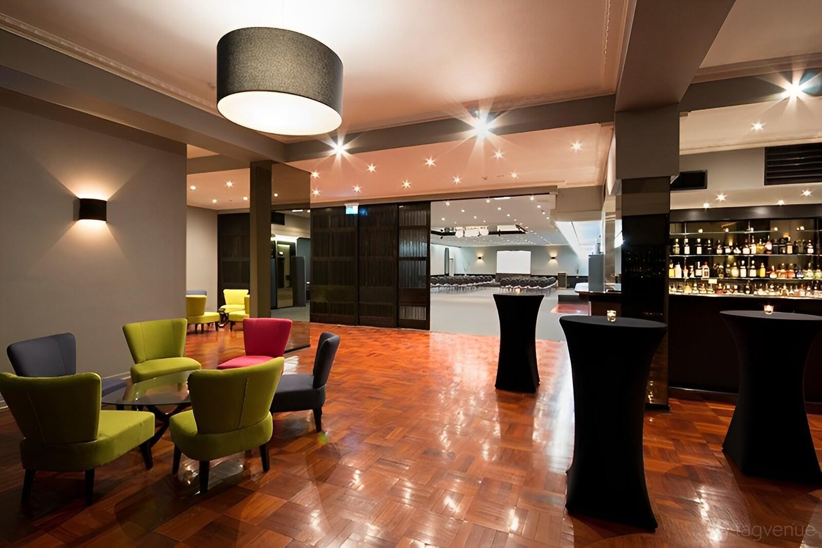 An event venue with parquet flooring, colorful lounge chairs, cocktail tables, and a stocked bar at Crest On Barkly.