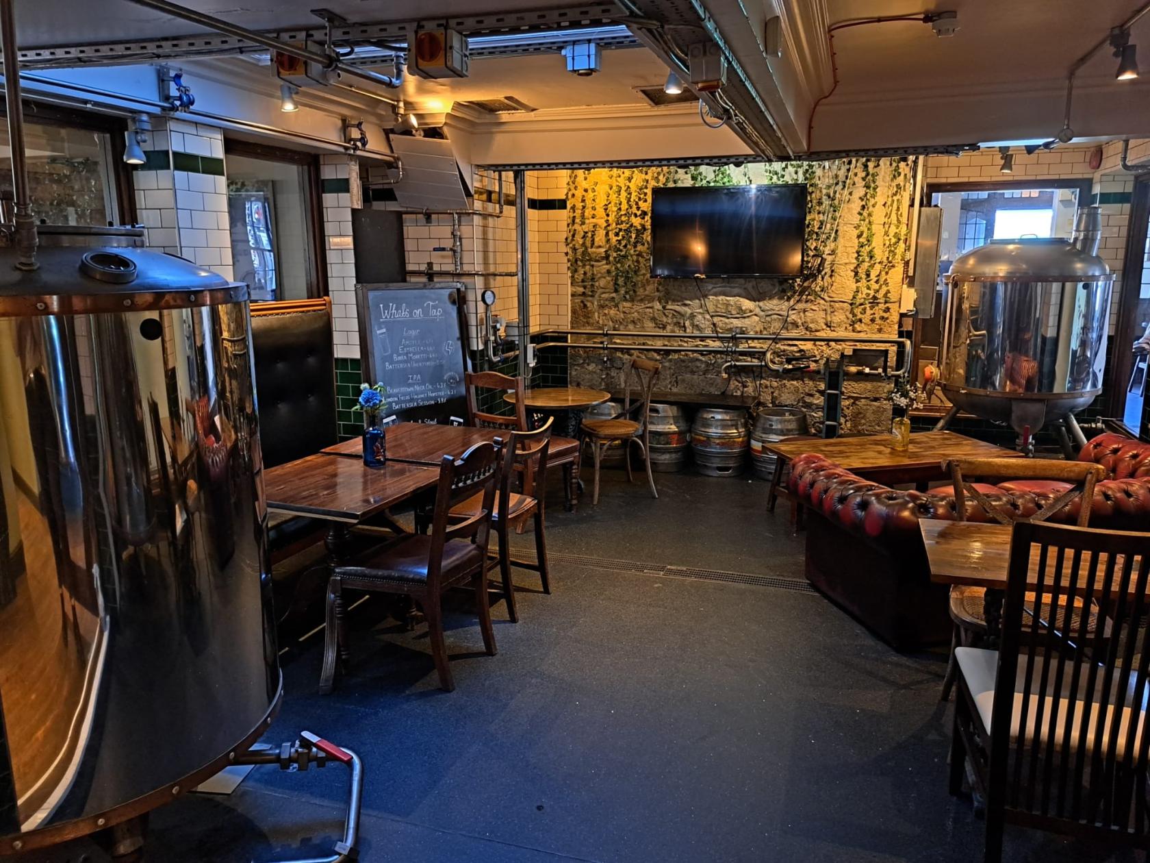 A bar with stainless steel brewing tanks, leather seating, and exposed stone walls at The Oak Tavern.