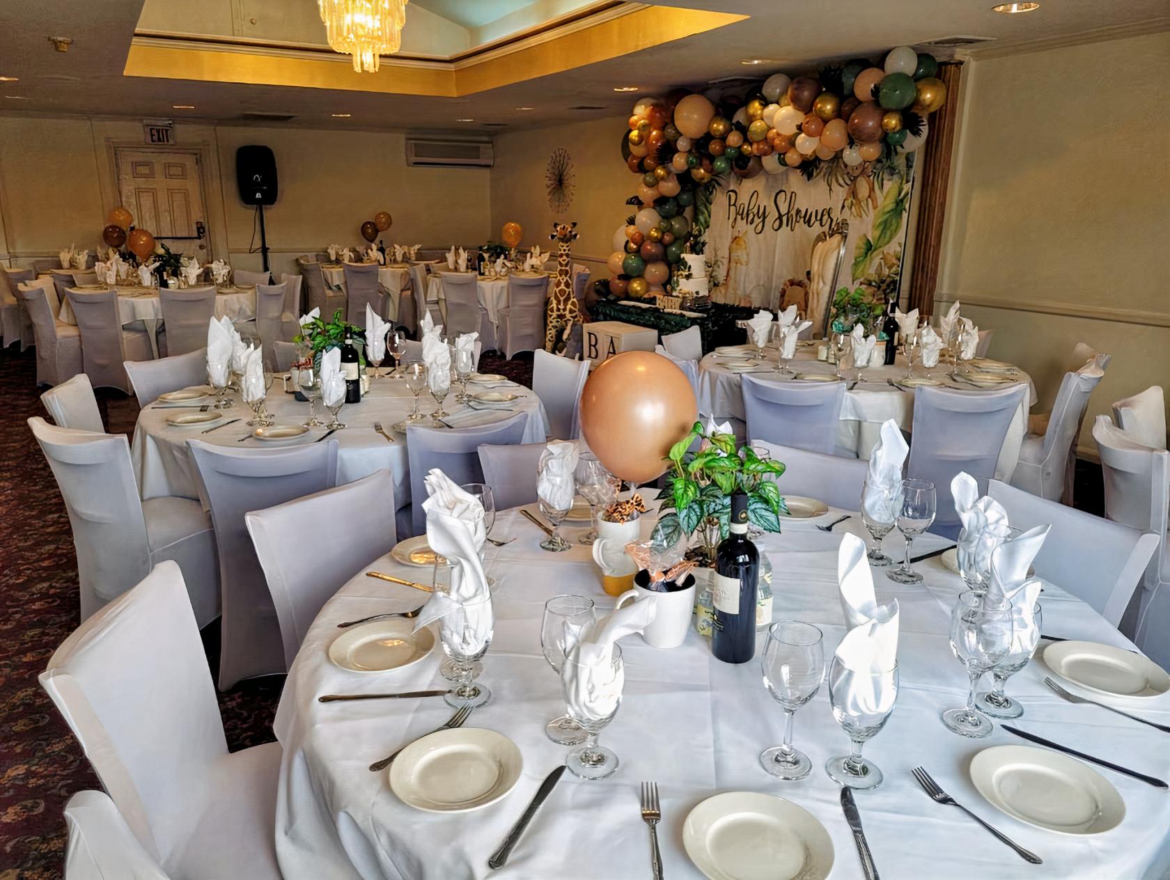 An upstairs event space with round tables draped in white linens, balloon decorations, and folded napkins at Tombolino Ristorante.