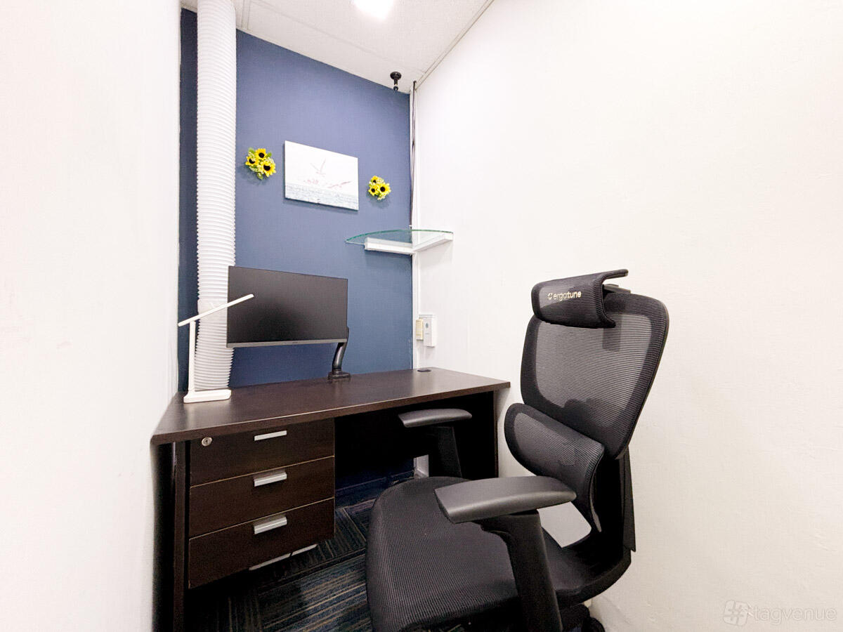 An office space with a single workstation, ergonomic chair, computer monitor, and decorative sunflowers at RoomKiosk Tanjong Pagar.