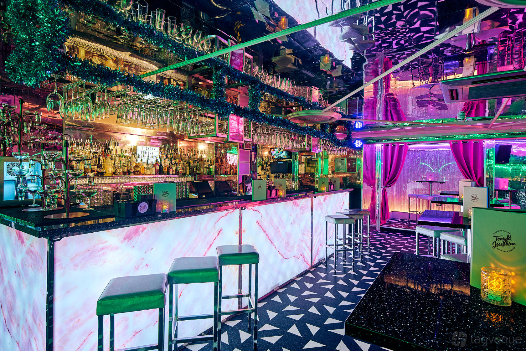 A cocktail bar with a marble-front counter, geometric tile flooring, mirrored ceiling, and colorful neon lighting at Tonight Josephine Shoreditch.