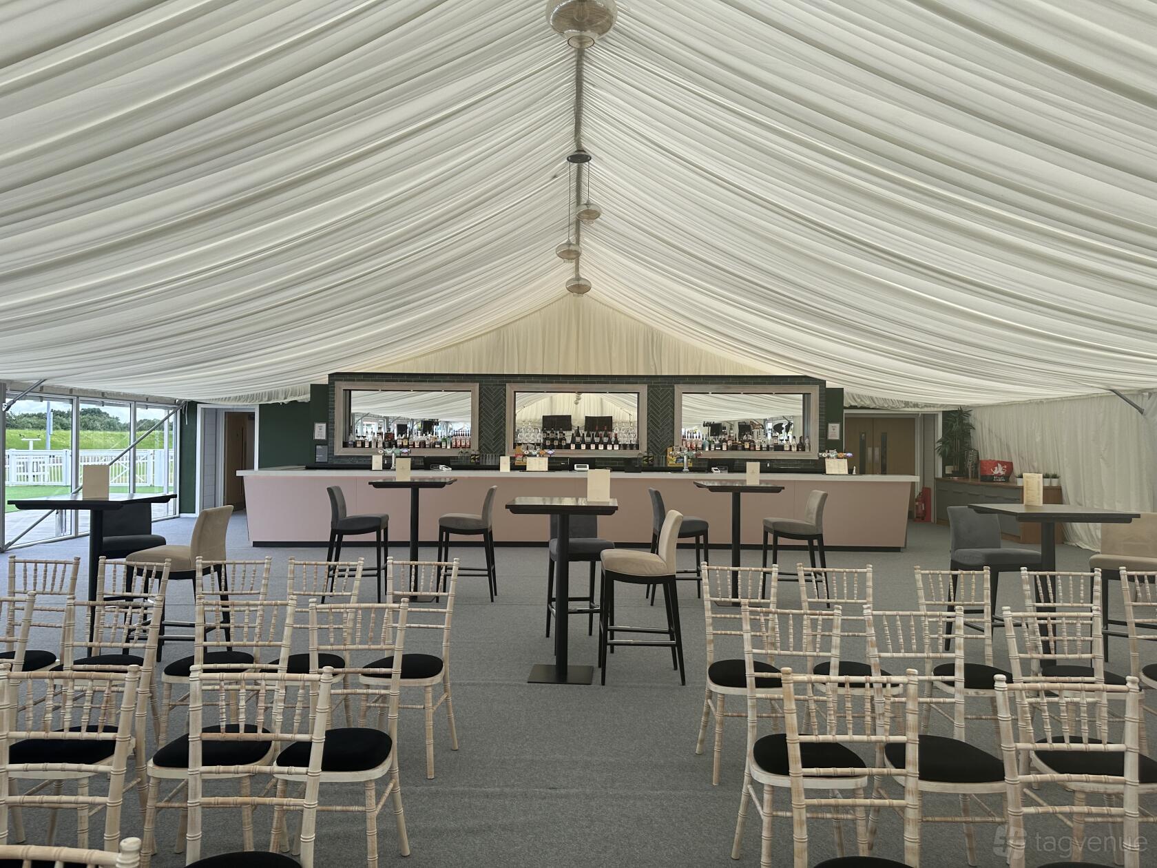 An event venue with a draped marquee ceiling, cocktail tables, and a mirrored bar at Chelmsford City Racecourse.