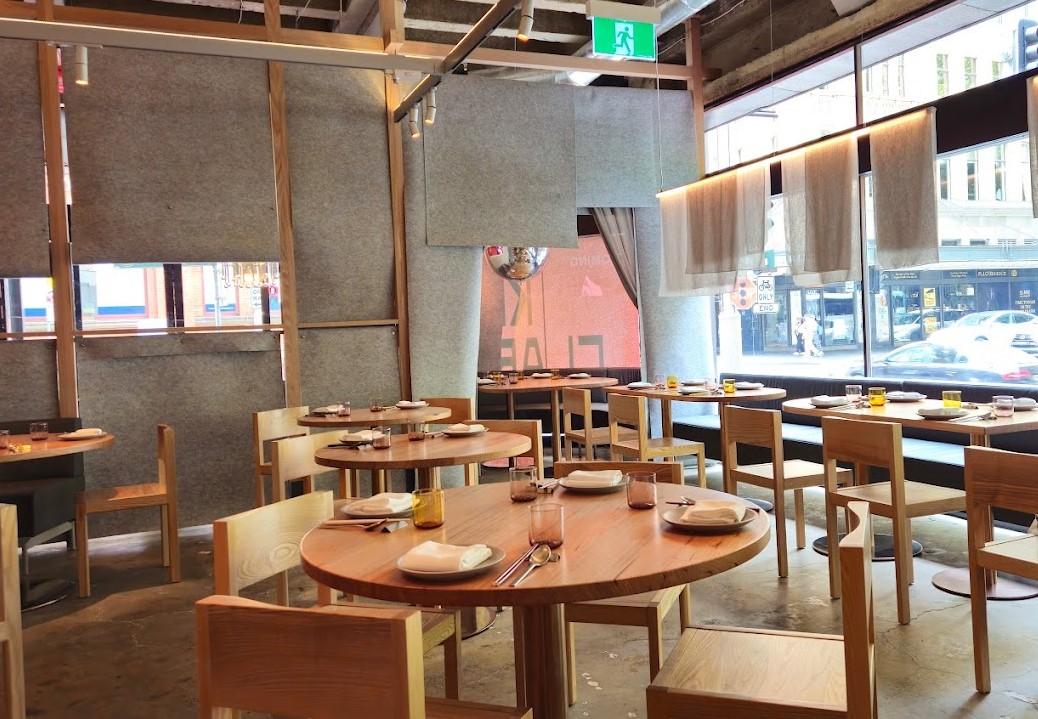 A restaurant with round wooden tables, minimalist chairs, floor-to-ceiling windows, and exposed ceiling at King Clarence.