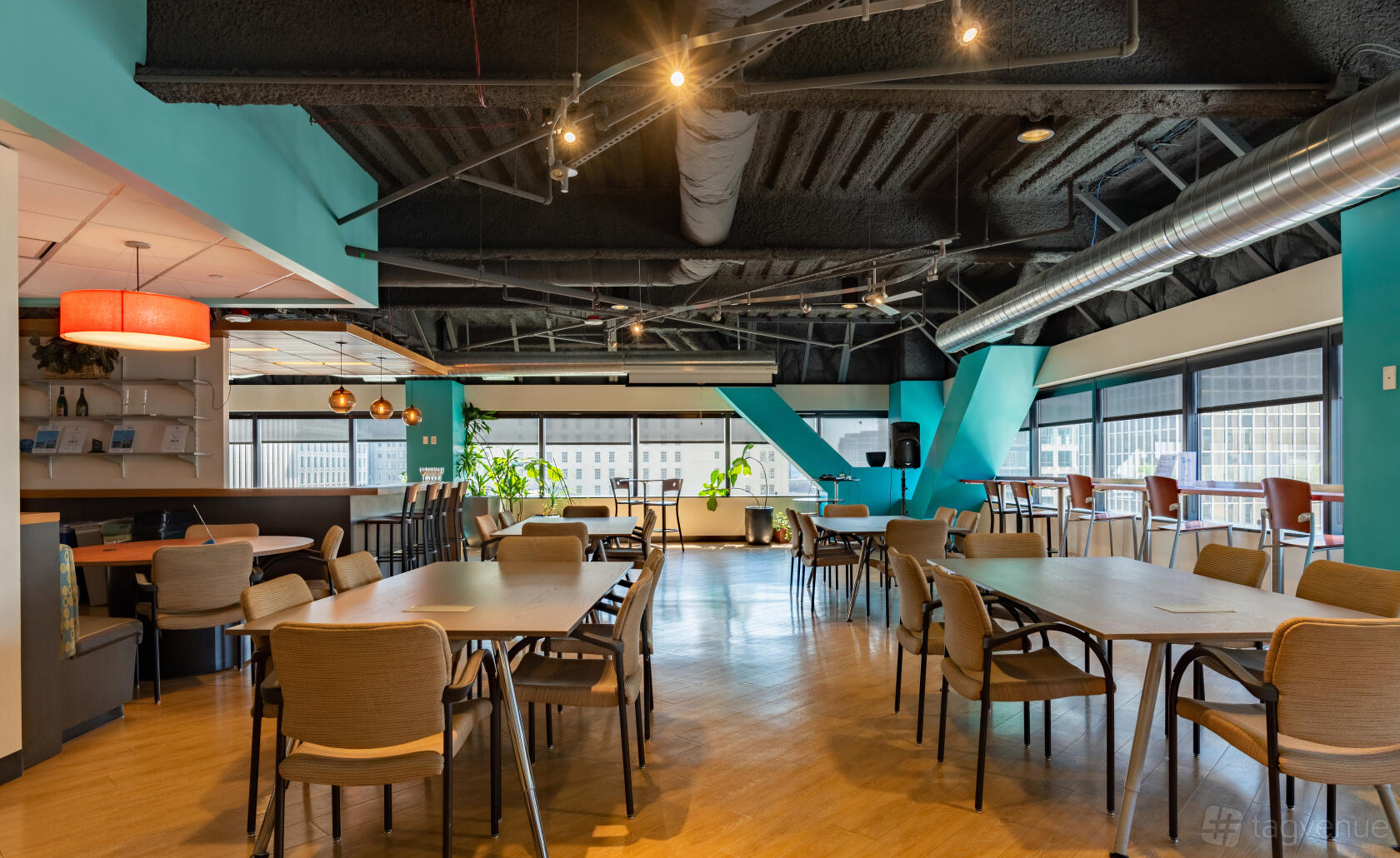 A coworking cafe with large windows, wooden tables, woven chairs, and teal accent walls at SURF Incubator.