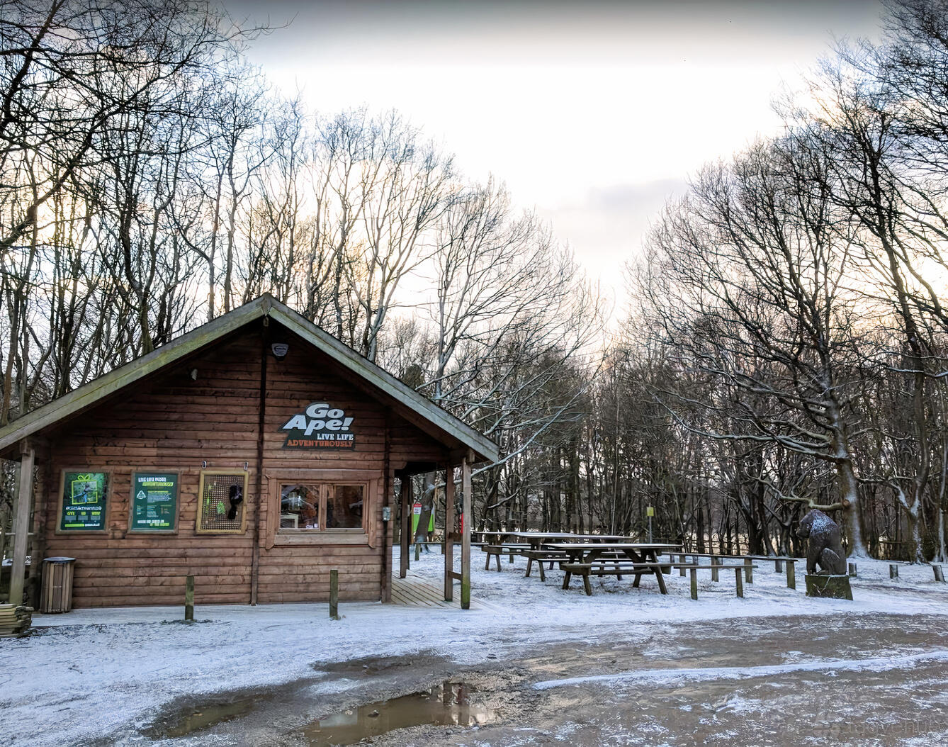 An outdoor venue with a wooden cabin, picnic tables, and snow-covered ground at Go Ape Rivington.