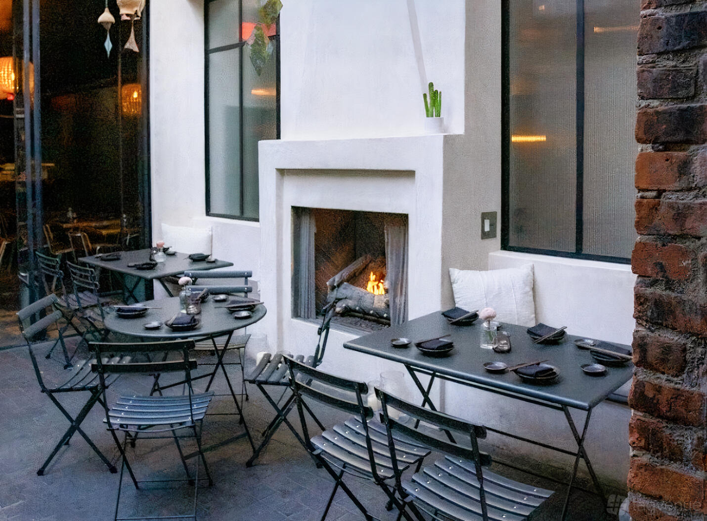 A restaurant terrace with black metal tables, folding chairs, and a lit fireplace at Ōwa.