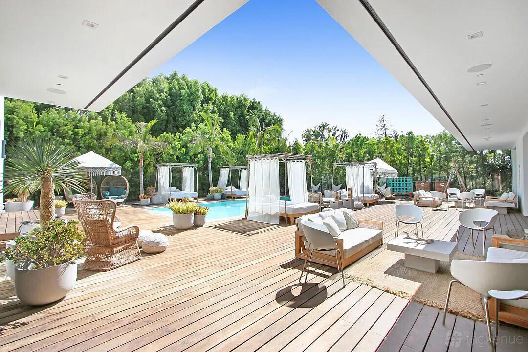 An apartment with a spacious wooden deck, poolside cabanas, wicker seating, and potted plants at Beautiful Sunset Mansion.