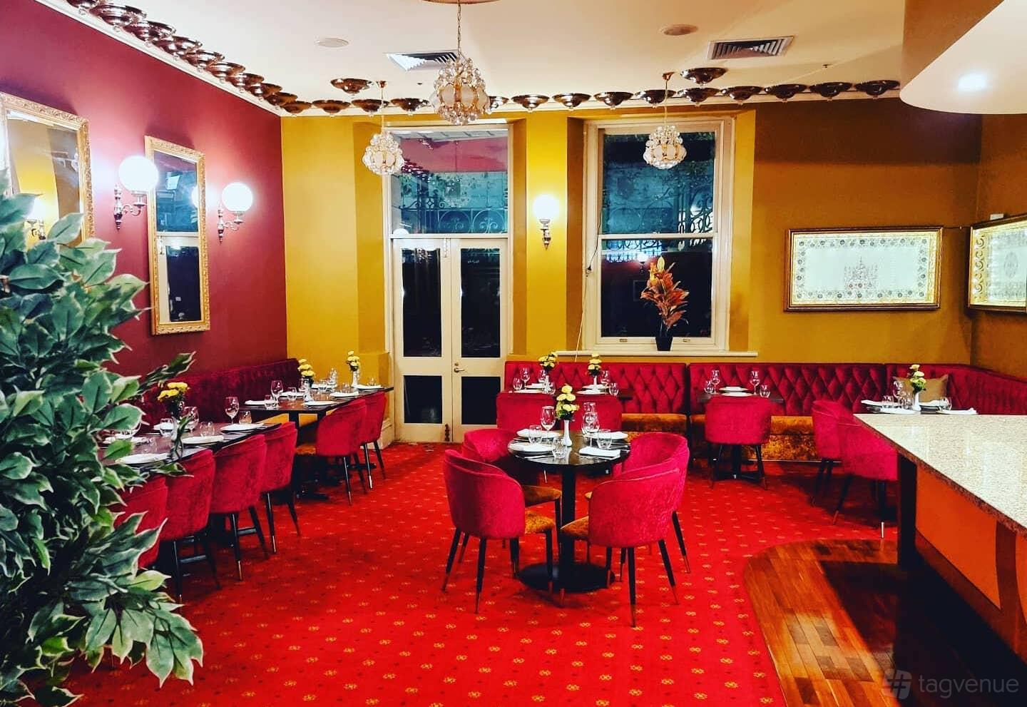 A function room with red upholstered chairs, patterned carpet, and wall sconces at Gaylord Indian Restaurant.