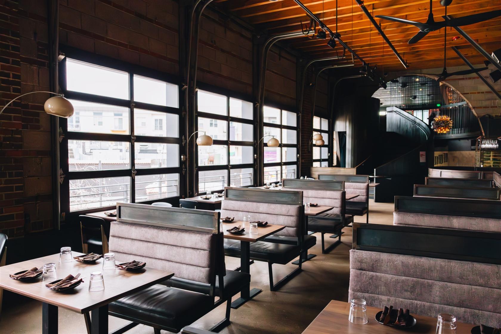 A restaurant with velvet booths, exposed brick, and large garage-style windows at Linger.