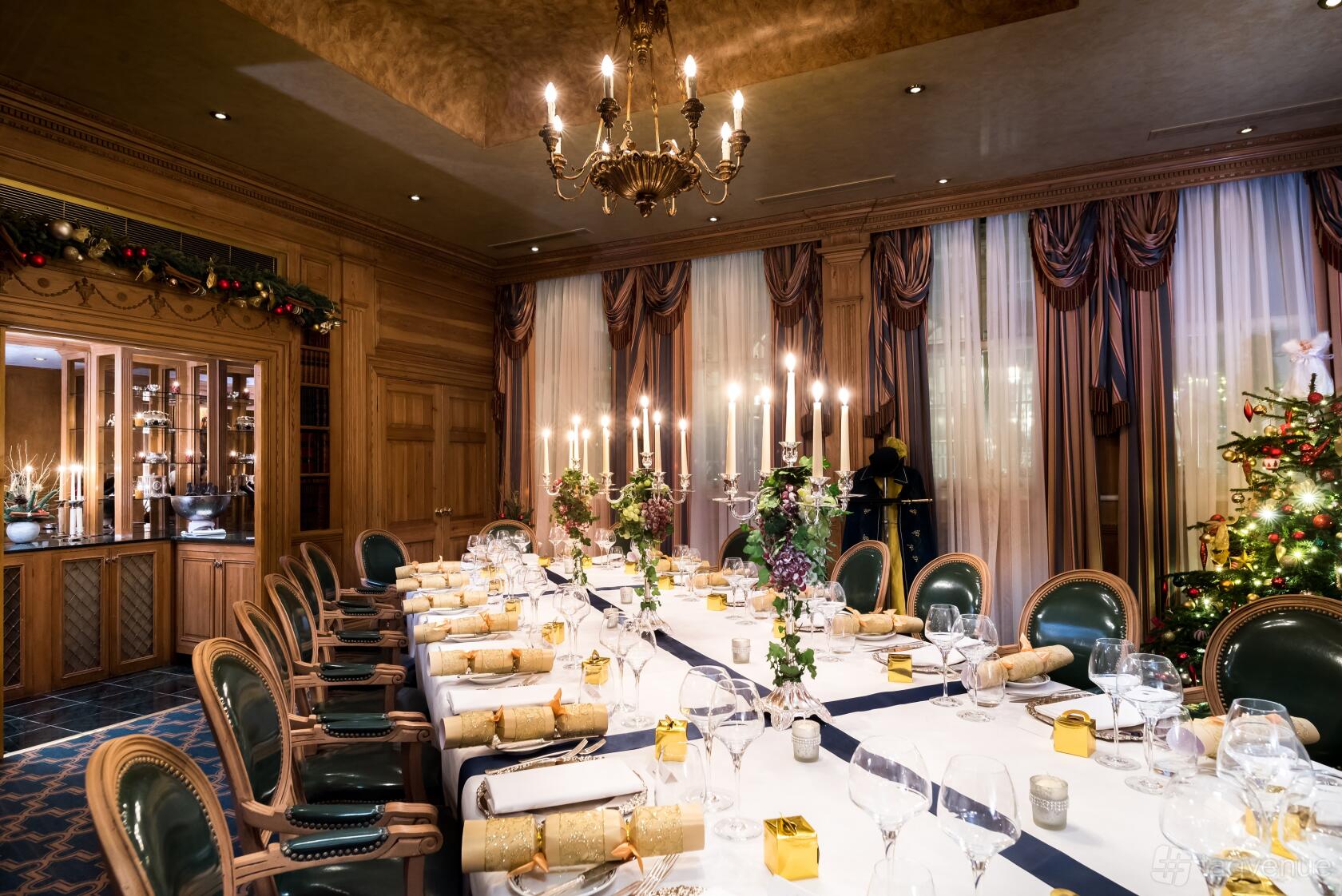 A dining room with a long banquet table, candle centerpieces, wood-paneled walls, and draped windows at The Milestone Hotel and Residences.