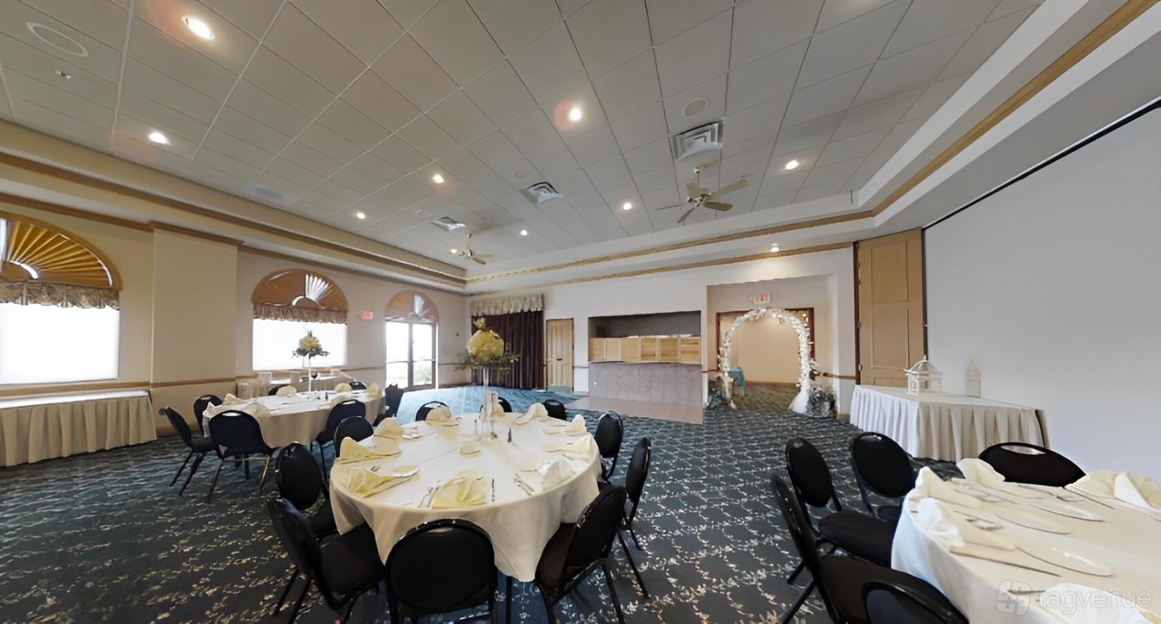 An event venue with round tables covered in white linens, carpeted floors, and an arched floral entryway at Jennifer's Garden.
