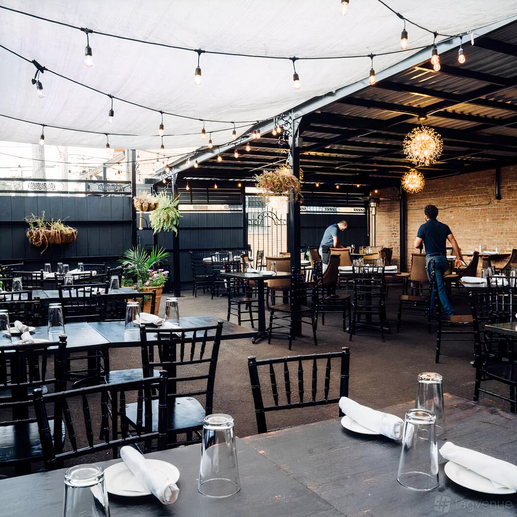 An outdoor dining area with black chairs, string lights, potted plants, and a partially covered patio at La Parra Restaurant & Bar.