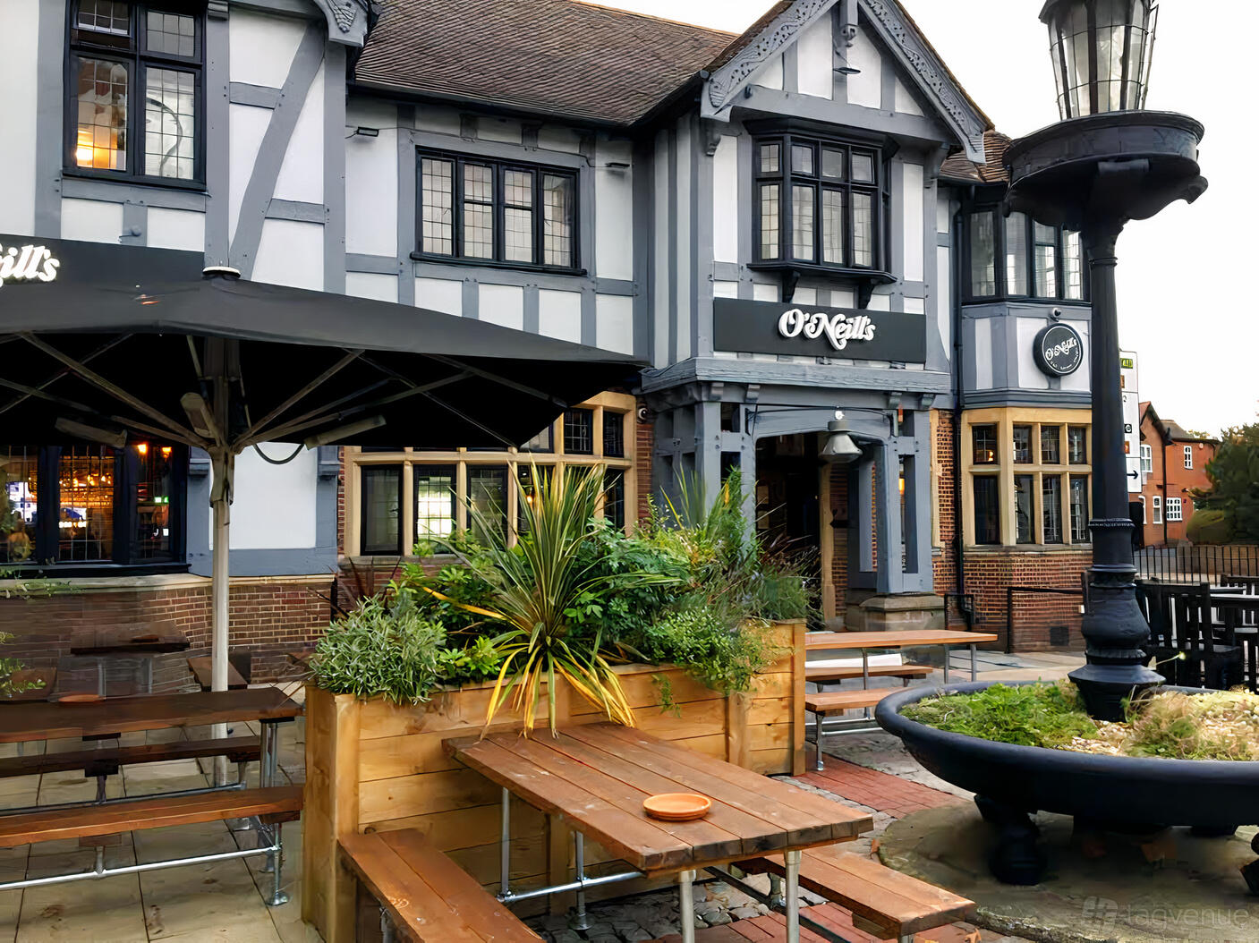 A pub with Tudor-style exterior, wooden picnic tables, large umbrellas, and planters at Arrowsmiths @ O'Neill's Solihull.