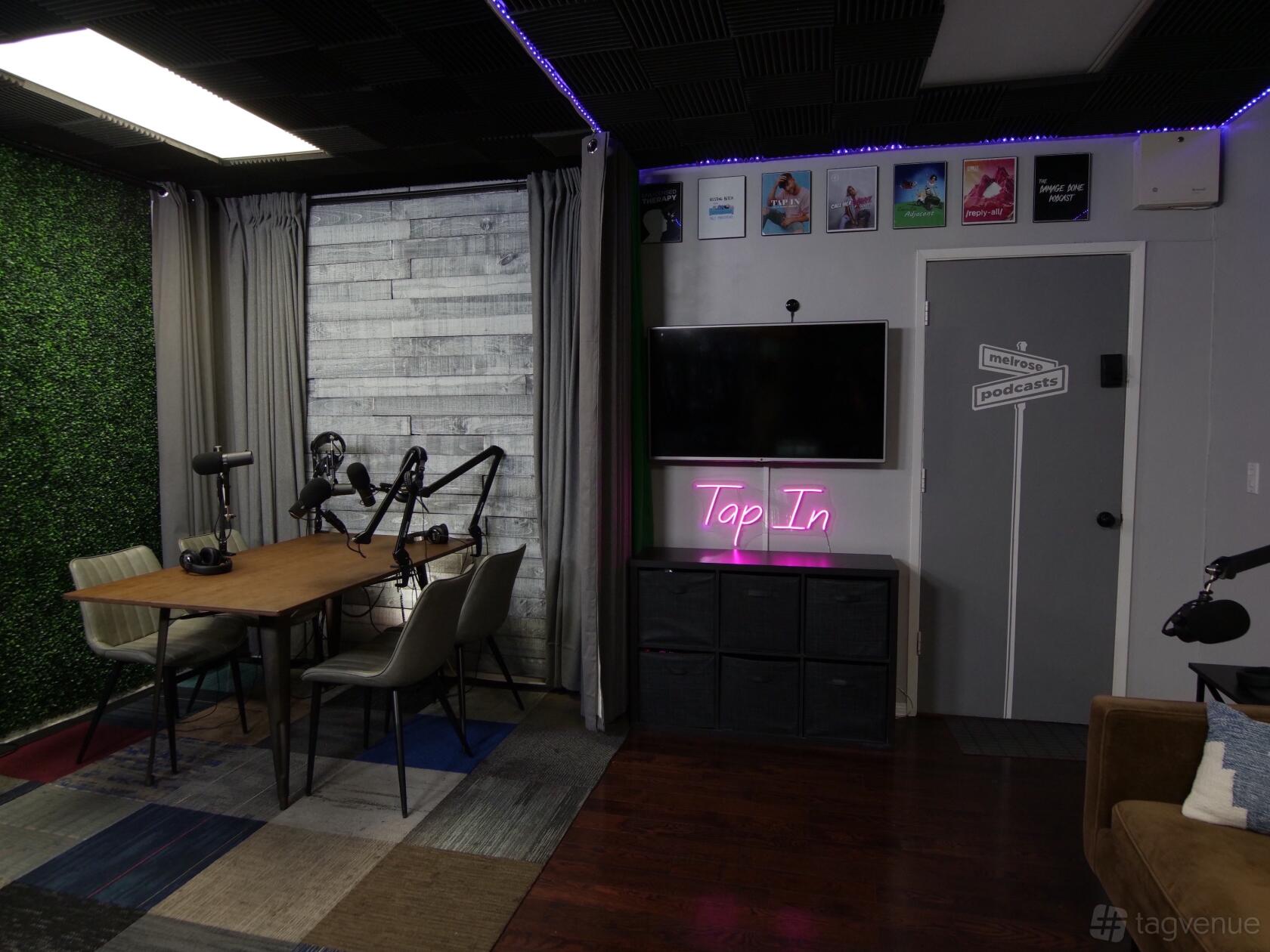 A podcast studio with a table, microphones, soundproofing, neon sign, and wall art at Melrose Podcasts.