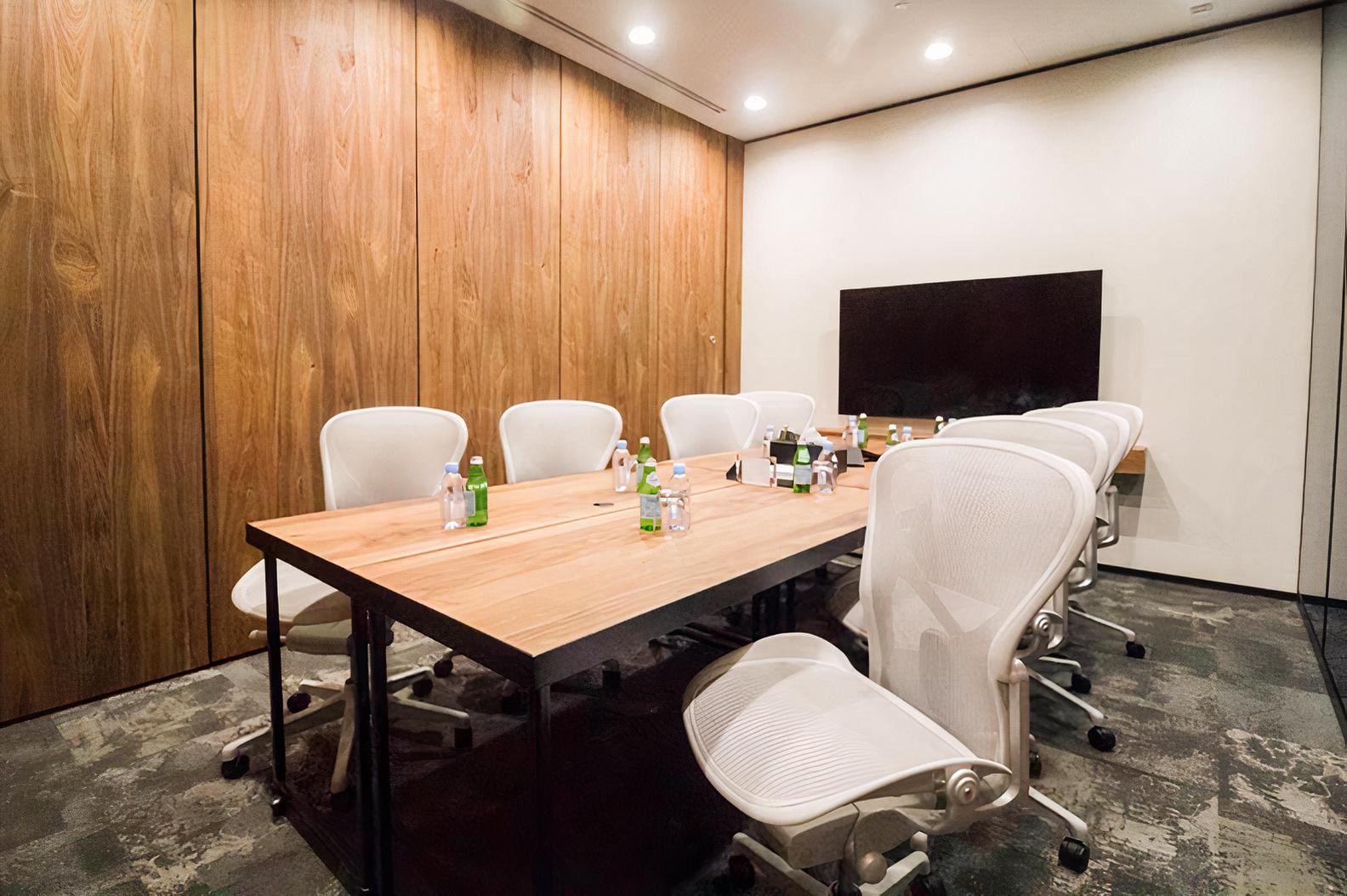 A coworking meeting room with a wooden table, white chairs, water bottles, and a large display screen at Frasers Tower.