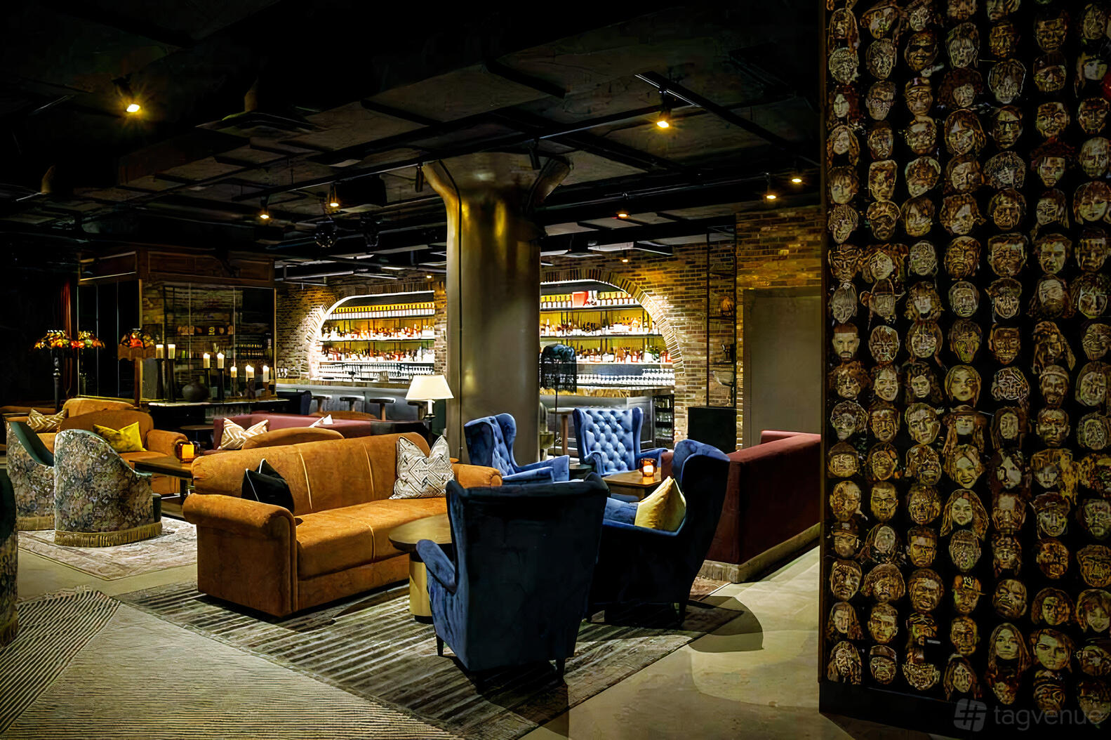 An event venue with eclectic lounge seating, exposed brick arches, and a wall covered in decorative masks at The Pearl.