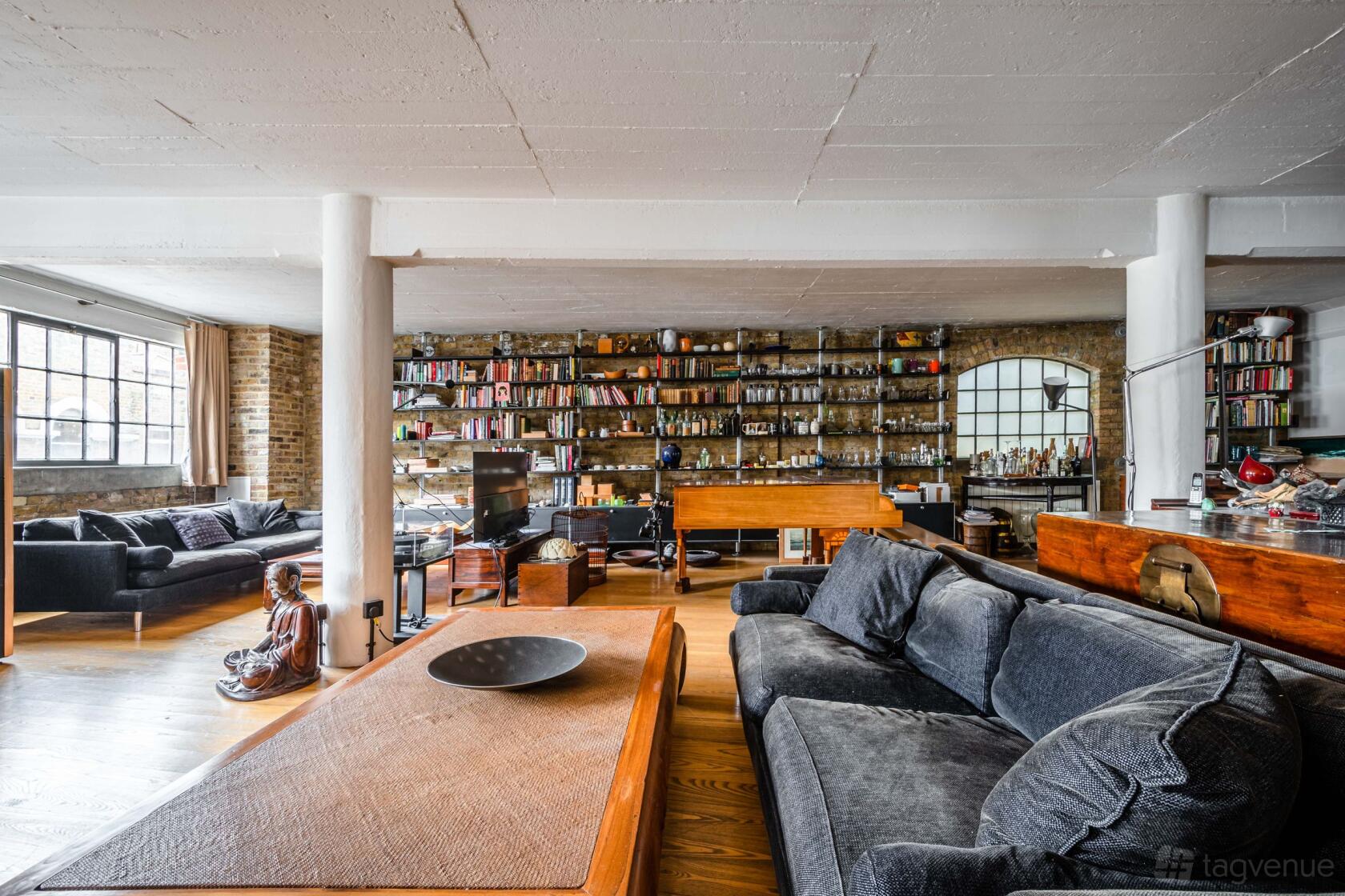 An event venue with exposed brick walls, large industrial windows, and shelves filled with books at Woolly Mammoth spaces London Bridge loft.
