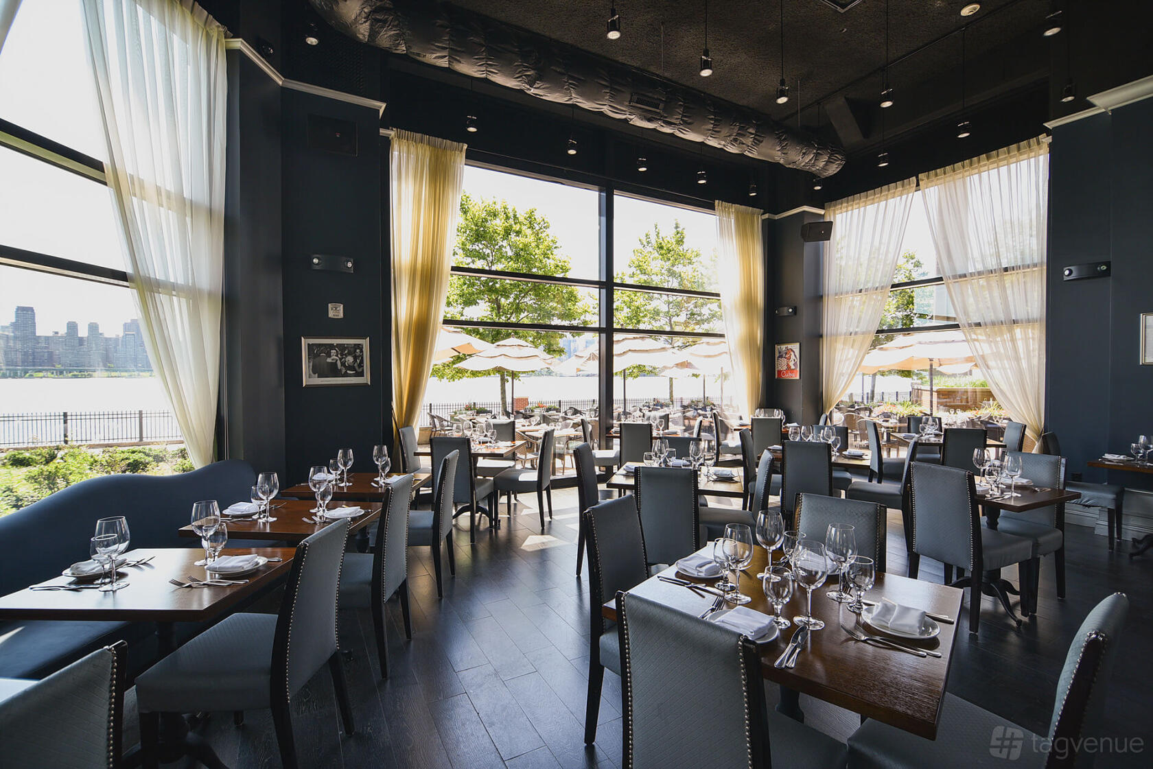 A restaurant dining room with floor-to-ceiling windows, natural light, and set tables at Son Cubano.