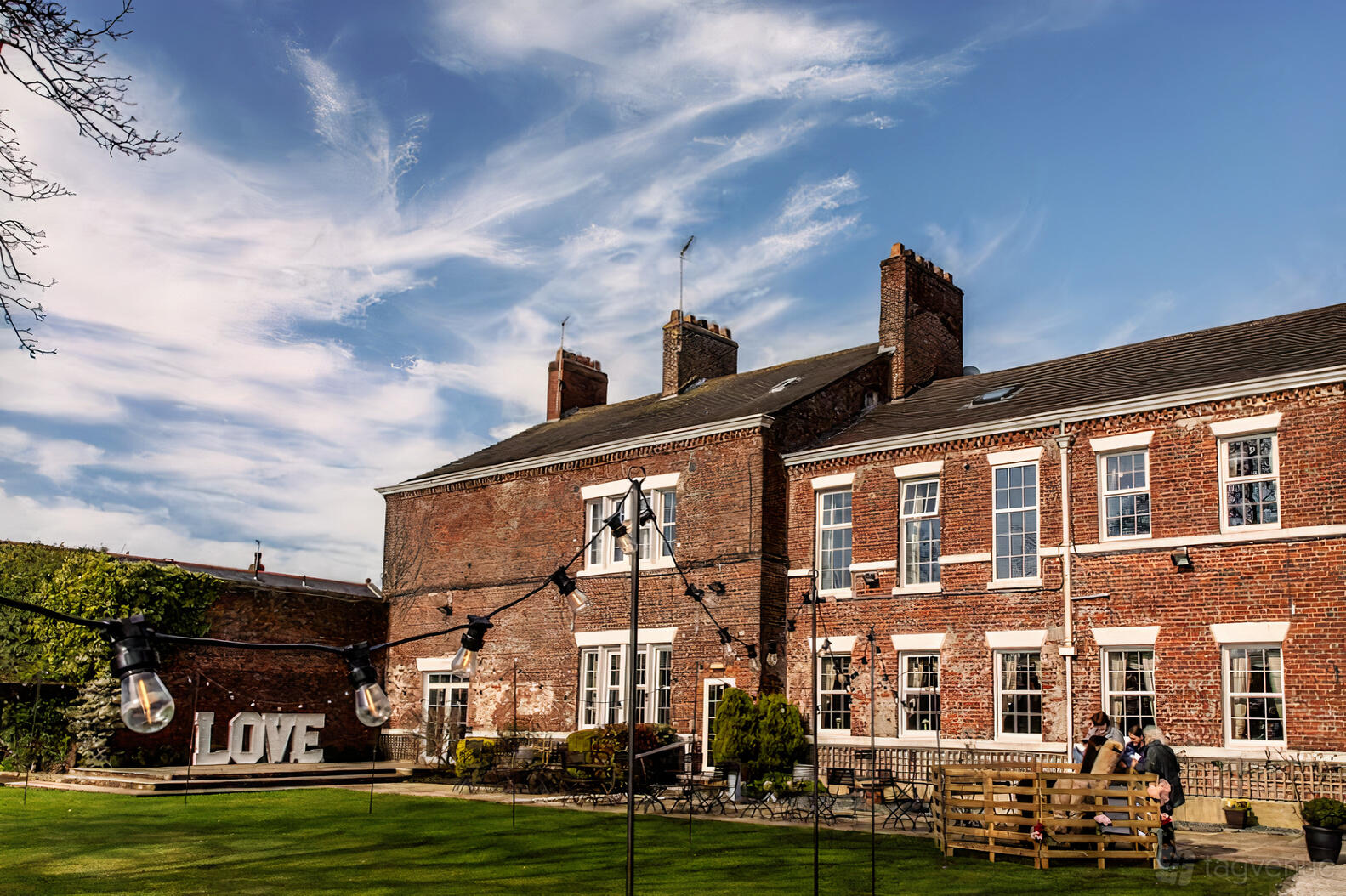 A country house with red brick exterior, outdoor string lights, and large white LOVE letters at Singleton Lodge Country House Hotel.