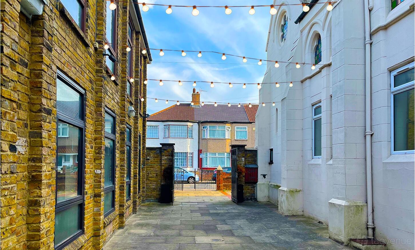An outdoor courtyard with string lights between brick and white church buildings at The Rock Event Space, Walthamstow.