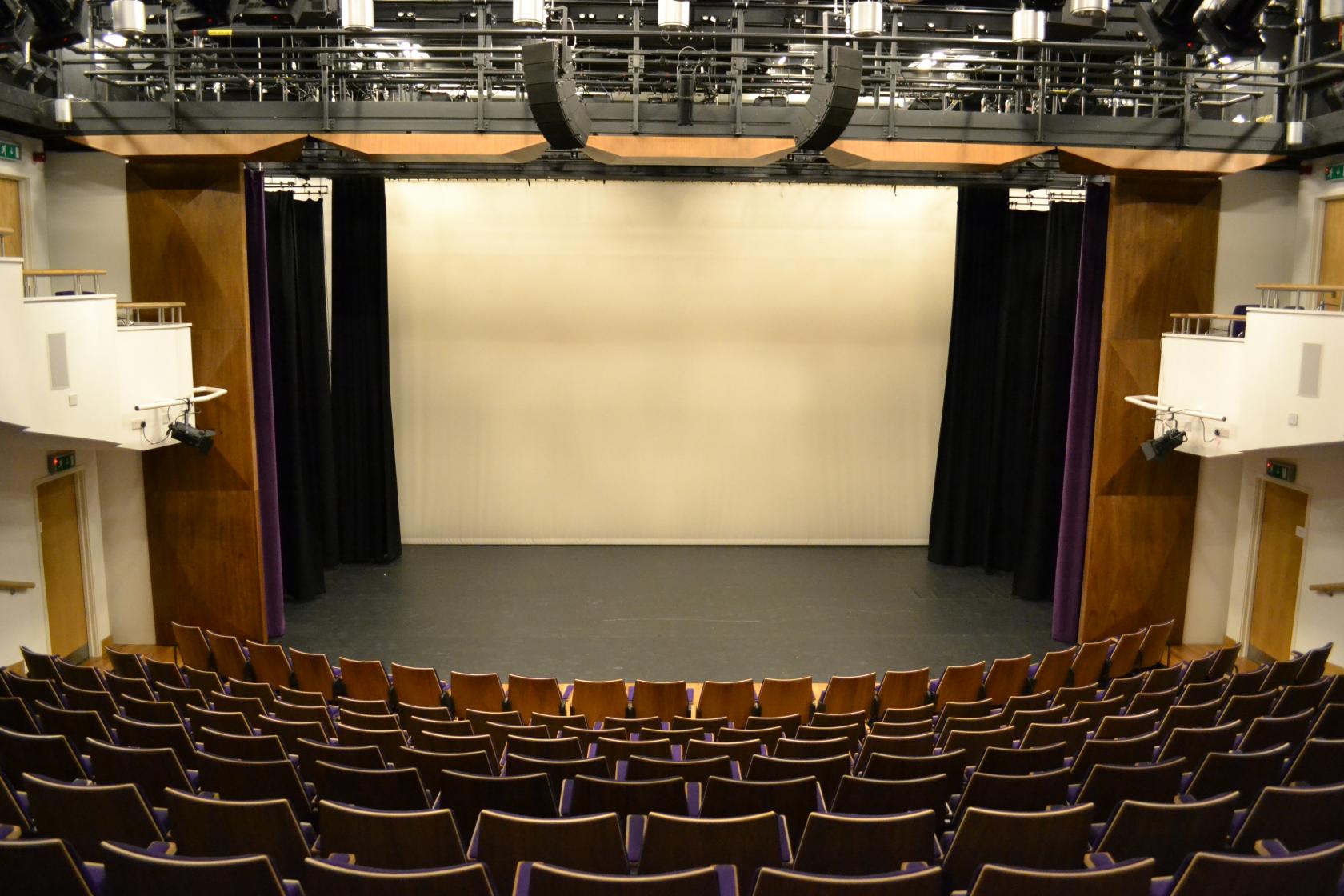 A theatre with tiered seating, a large stage, and overhead rigging at Creative Campus.