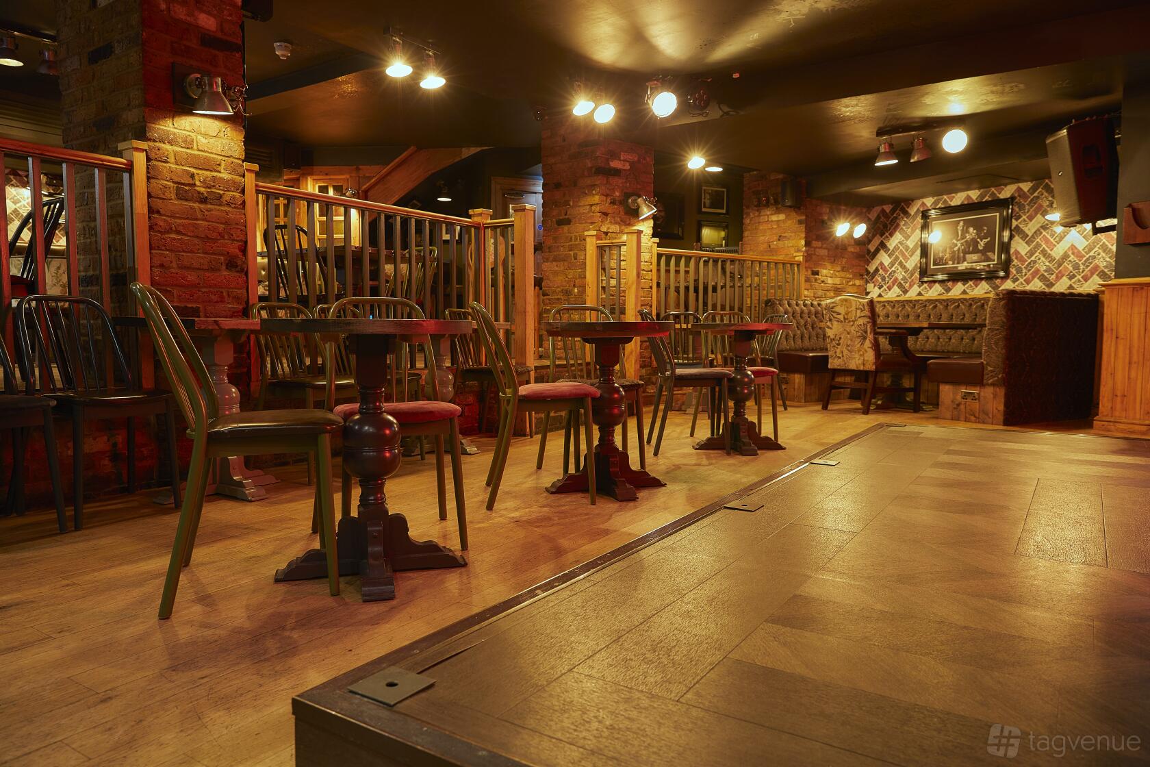A basement pub with exposed brick walls, wooden tables and chairs, and ambient lighting at The Spice of Life - Soho.