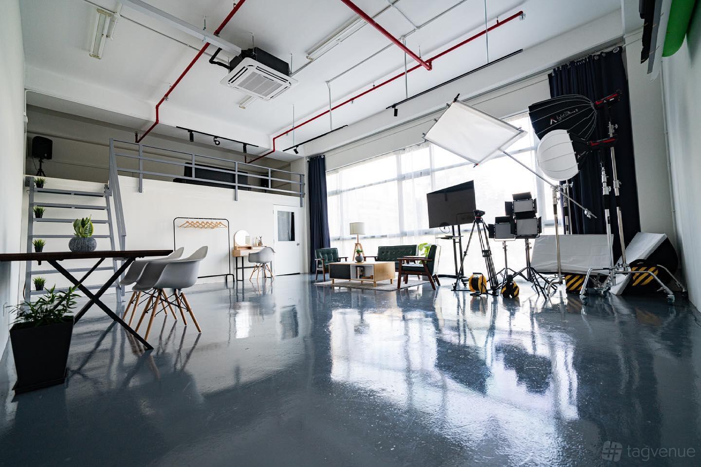 A photo studio with glossy floors, large windows, studio lighting equipment, and a mezzanine at Haste Studio by The Studio Clan.