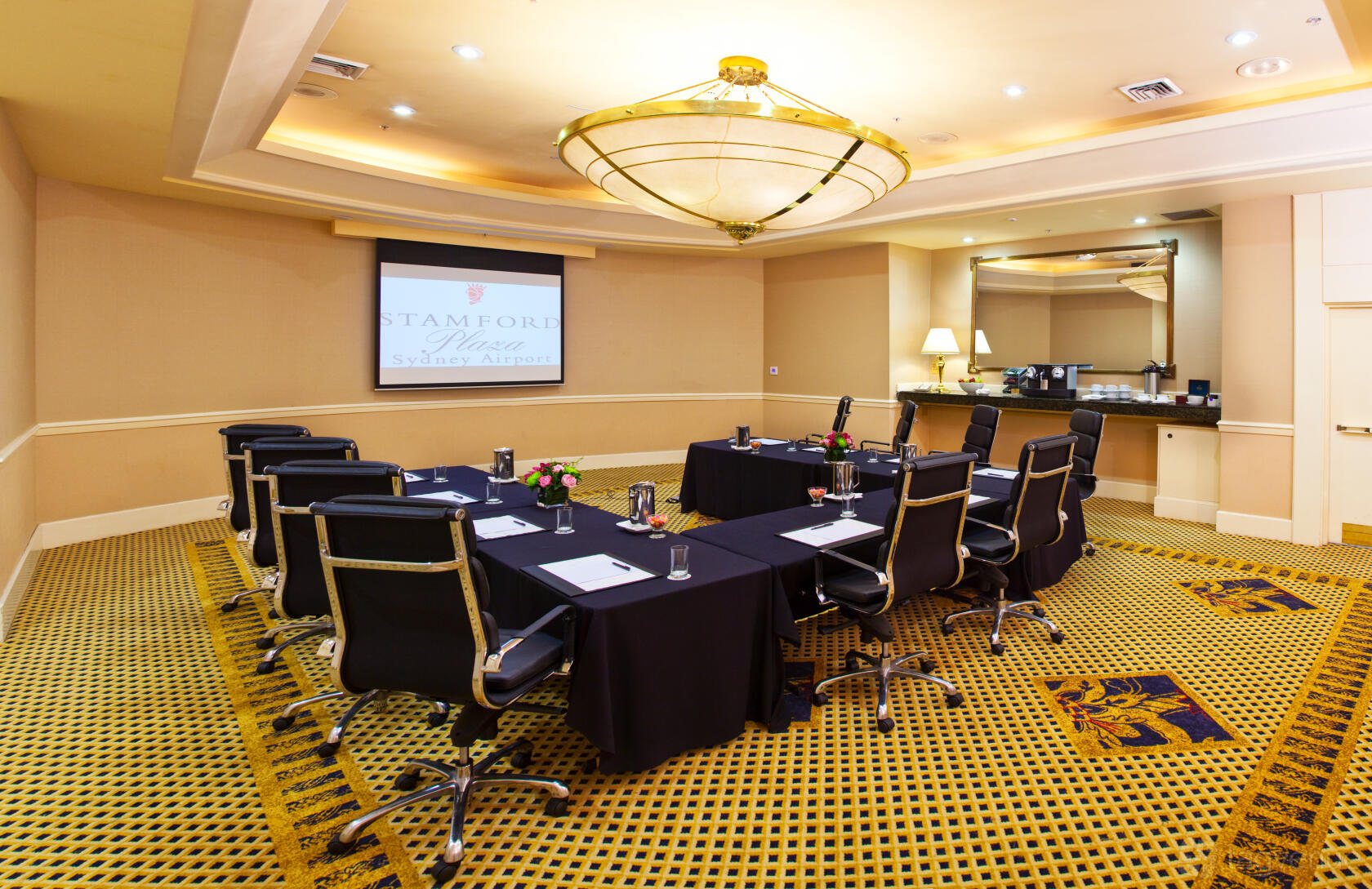A meeting room with a U-shaped table setup, executive chairs, and a ceiling chandelier at Stamford Plaza Sydney Airport Hotel.