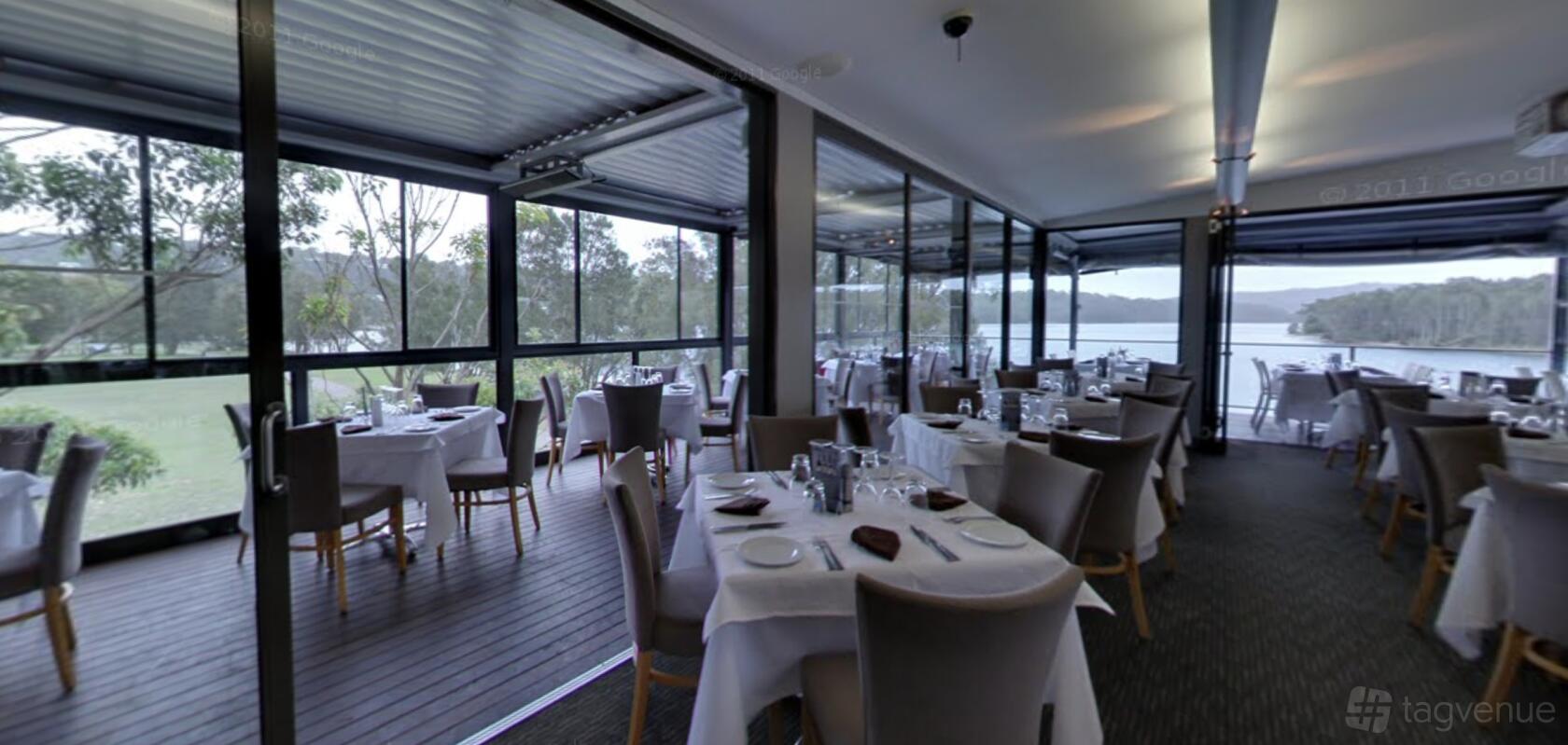 A restaurant with floor-to-ceiling windows, riverside views, and round tables with white linens at Limani Seafood Restaurant.