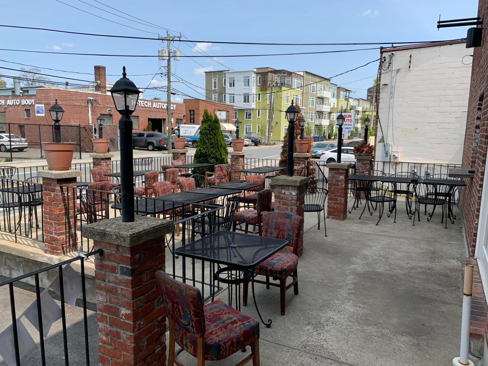 An outdoor terrace with wrought iron tables, patterned chairs, and brick columns at Lavash Bar & Grille.