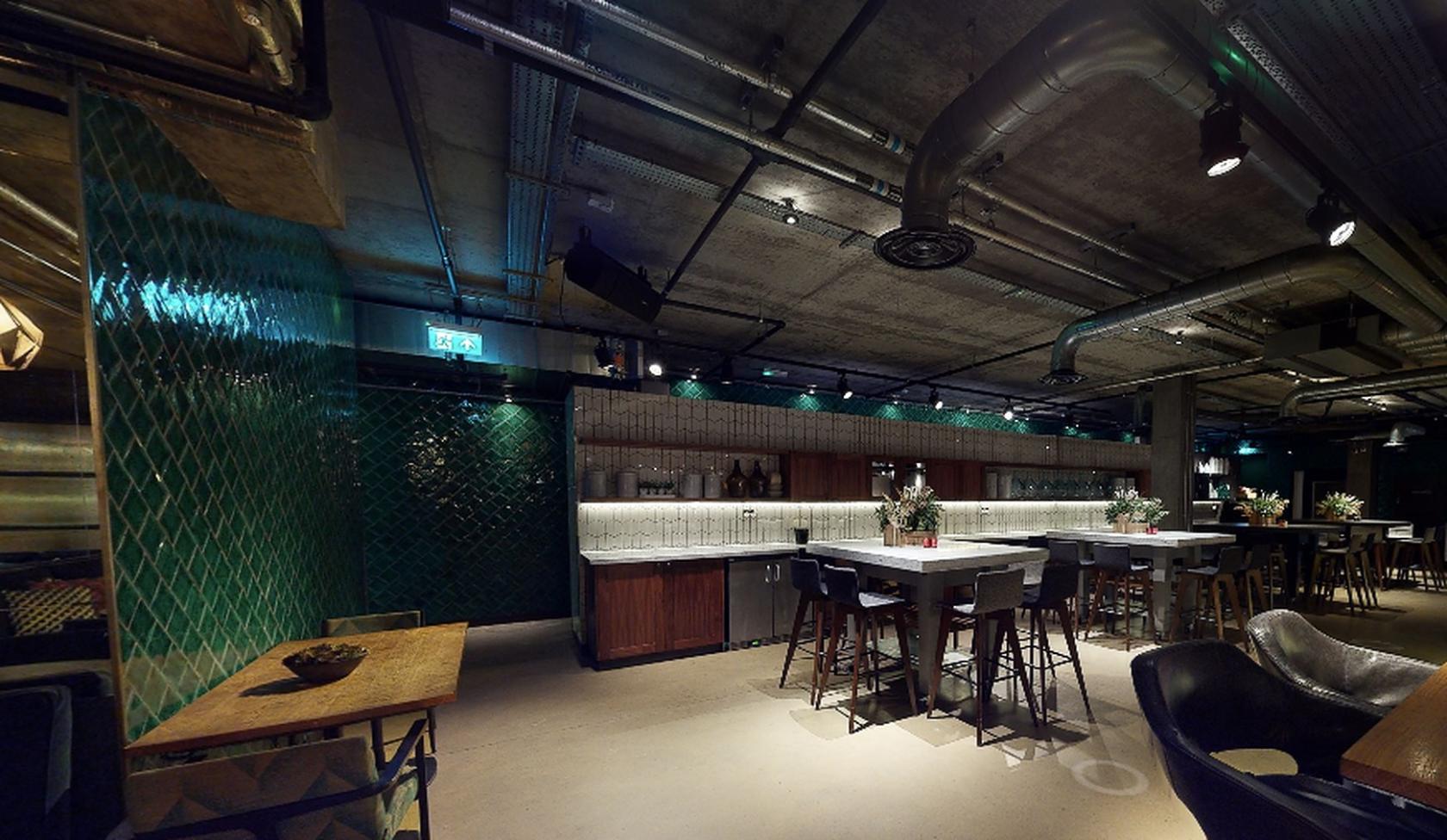 A bar with green tiled walls, industrial ceilings, and marble-topped high tables at Drake & Morgan at King's Cross.