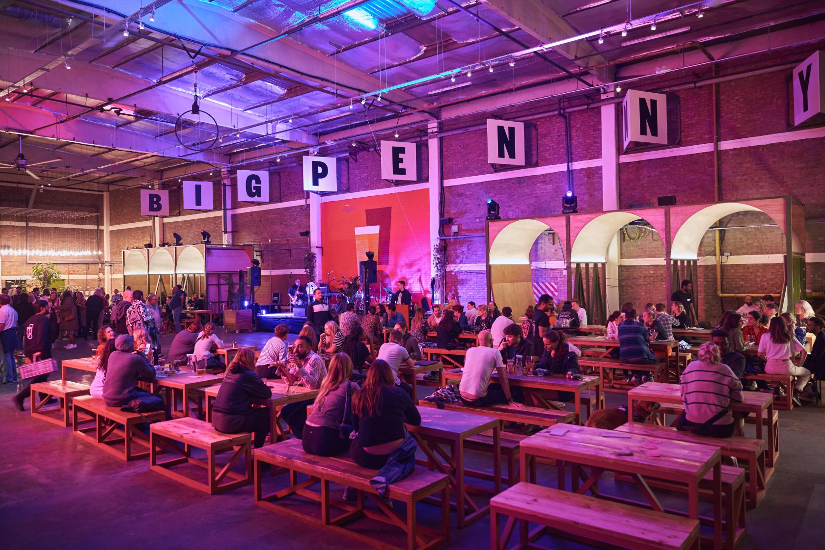 An event venue with long wooden tables, exposed brick walls, and stage lighting at Big Penny Social.