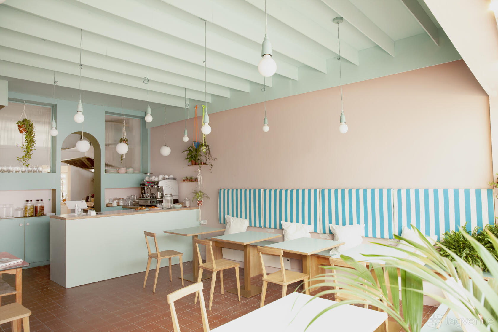 A cafe with pastel walls, wooden chairs, striped banquette seating, and hanging pendant lights at Kinder Kitchen Cafe.