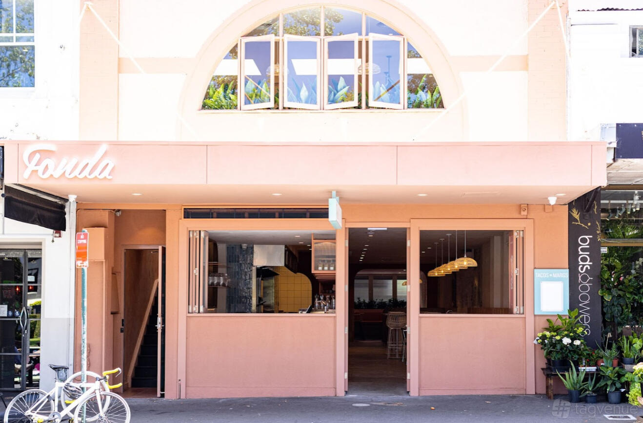 A restaurant with a pink exterior, large arched window, and open street-facing windows at Fonda Mexican @ Surry Hills.