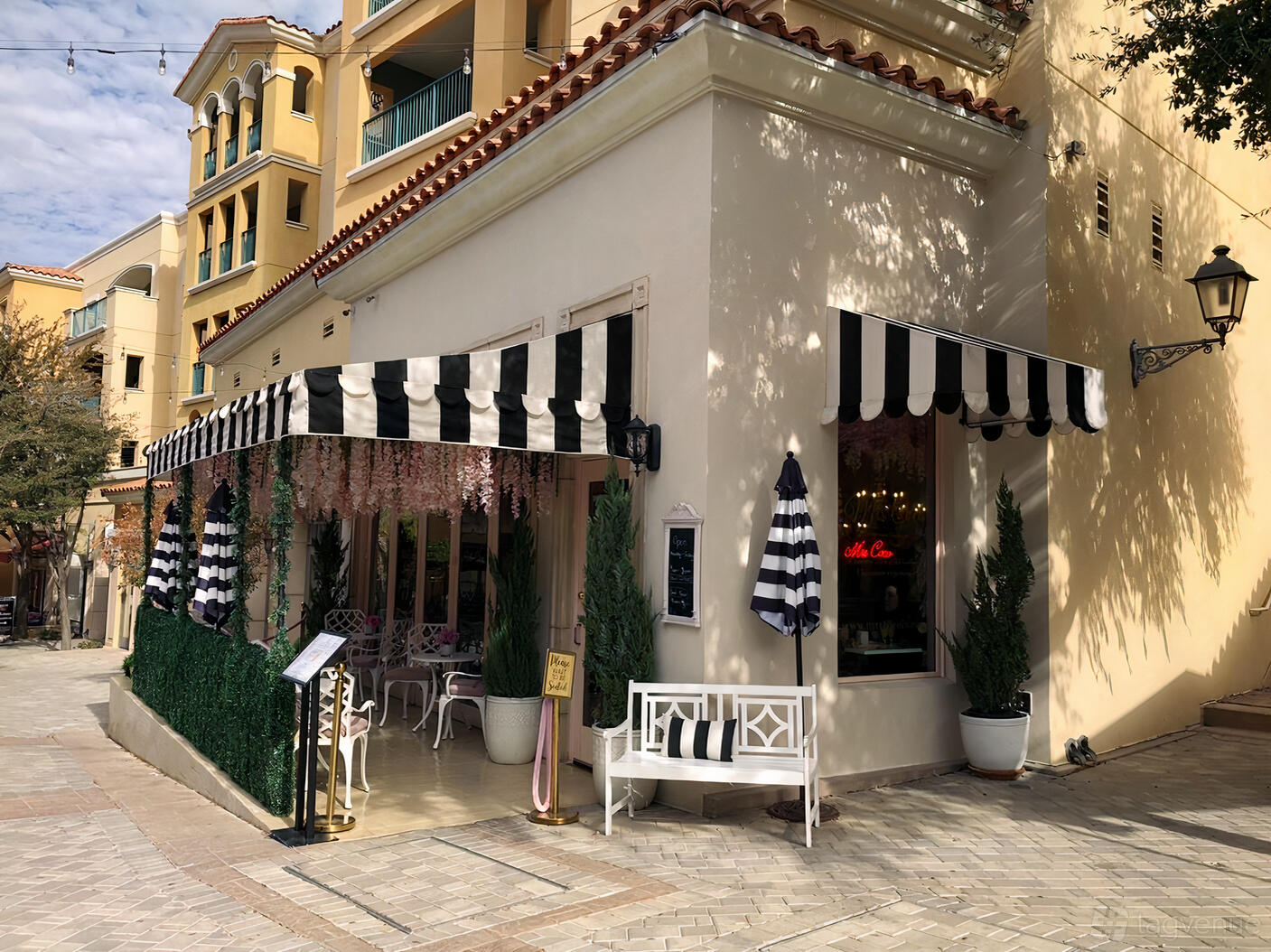 A café with striped awnings, pink floral decor, and outdoor benches at Mrs. Coco Cafe.