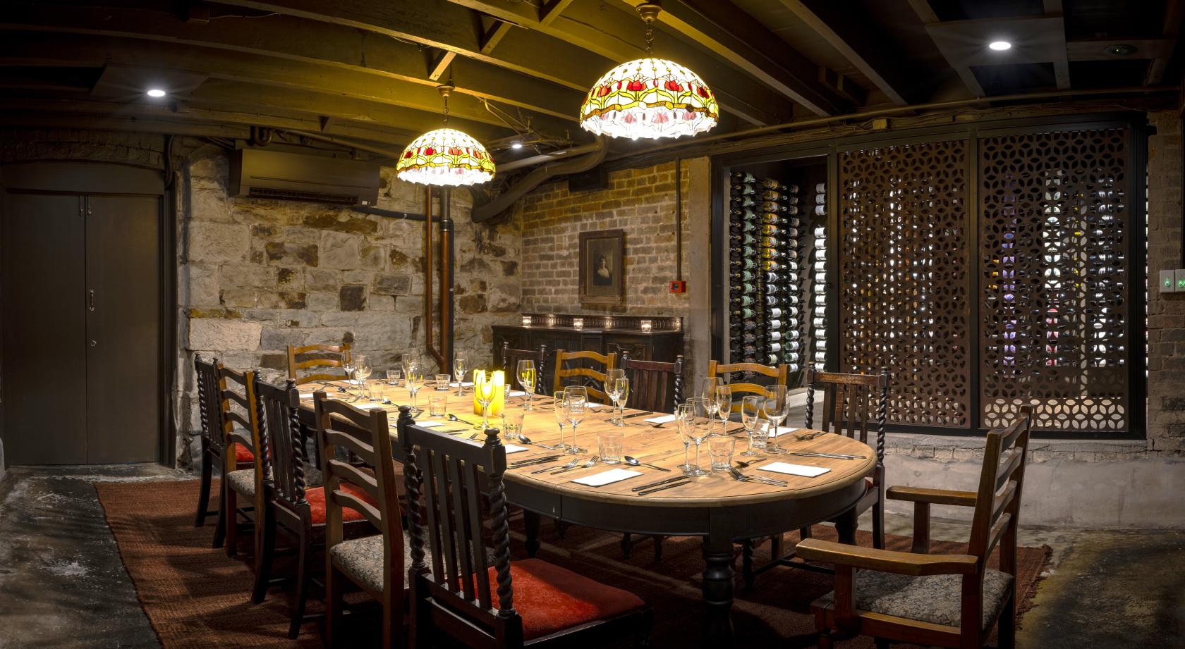 A dining room in a pub with exposed stone walls, wooden beams, and stained glass pendant lights at The Alliance Hotel.