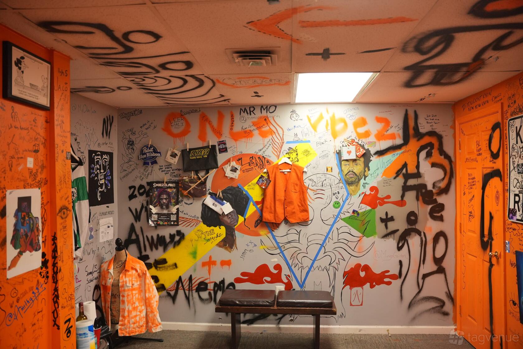 An art studio with graffiti-covered walls, hand-painted murals, and hanging orange jackets at Onle Vibez.
