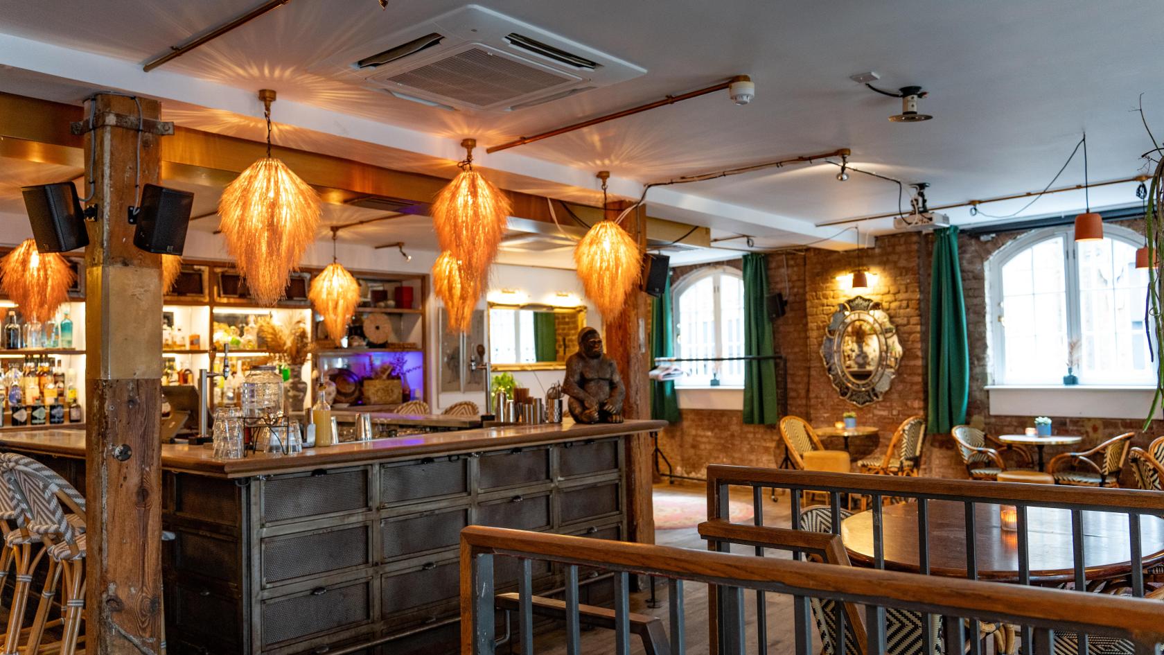 An event space in a restaurant with exposed brick walls, rattan pendant lights, and large windows at The Last Talisman.