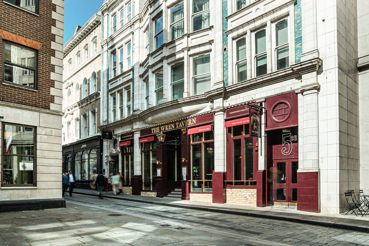 A pub with a classic red and gold facade, large windows, and stone street frontage at The Wren Tavern.