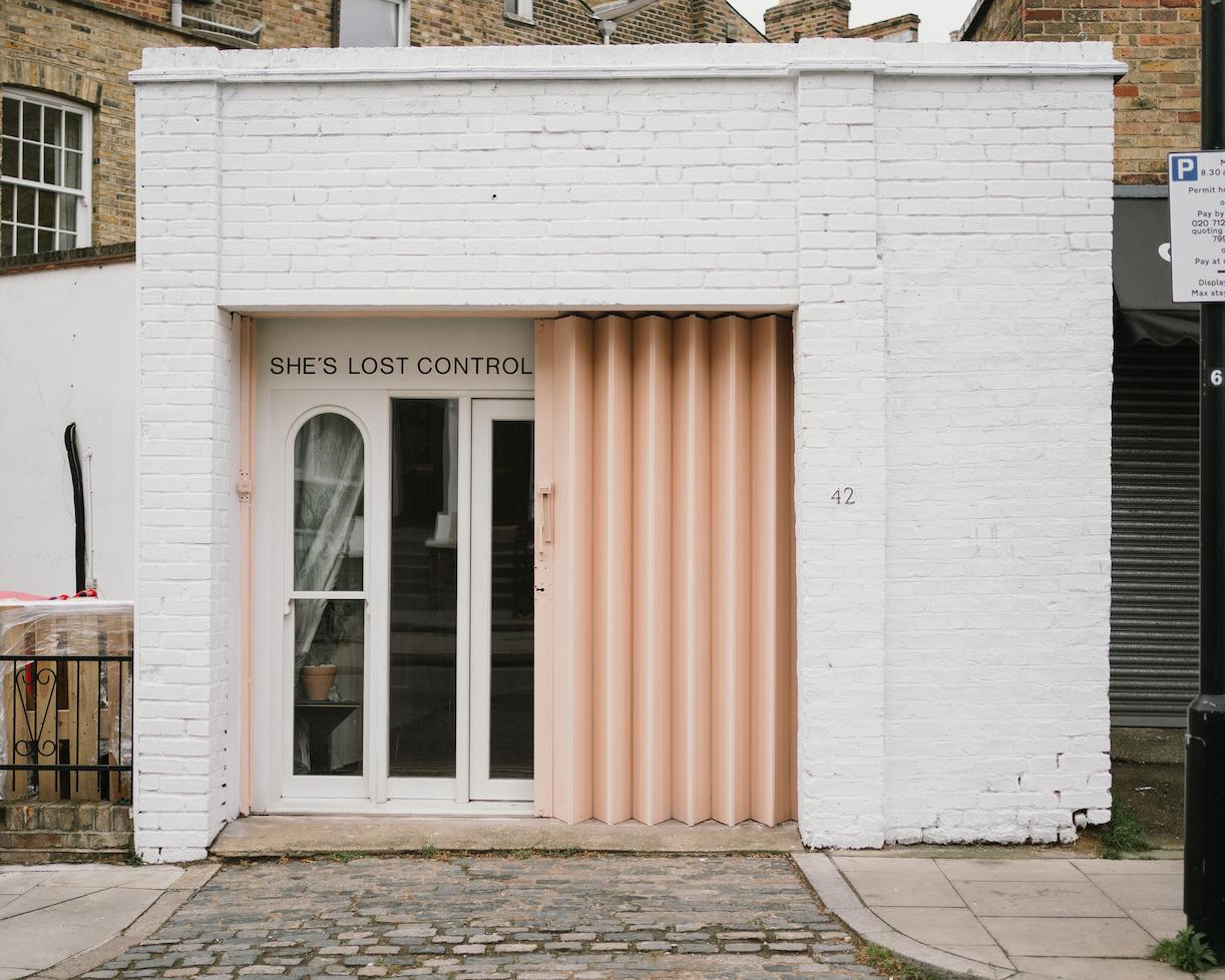 A versatile event space with a white brick facade, pink corrugated entryway, and arched windows at She's Lost Control.