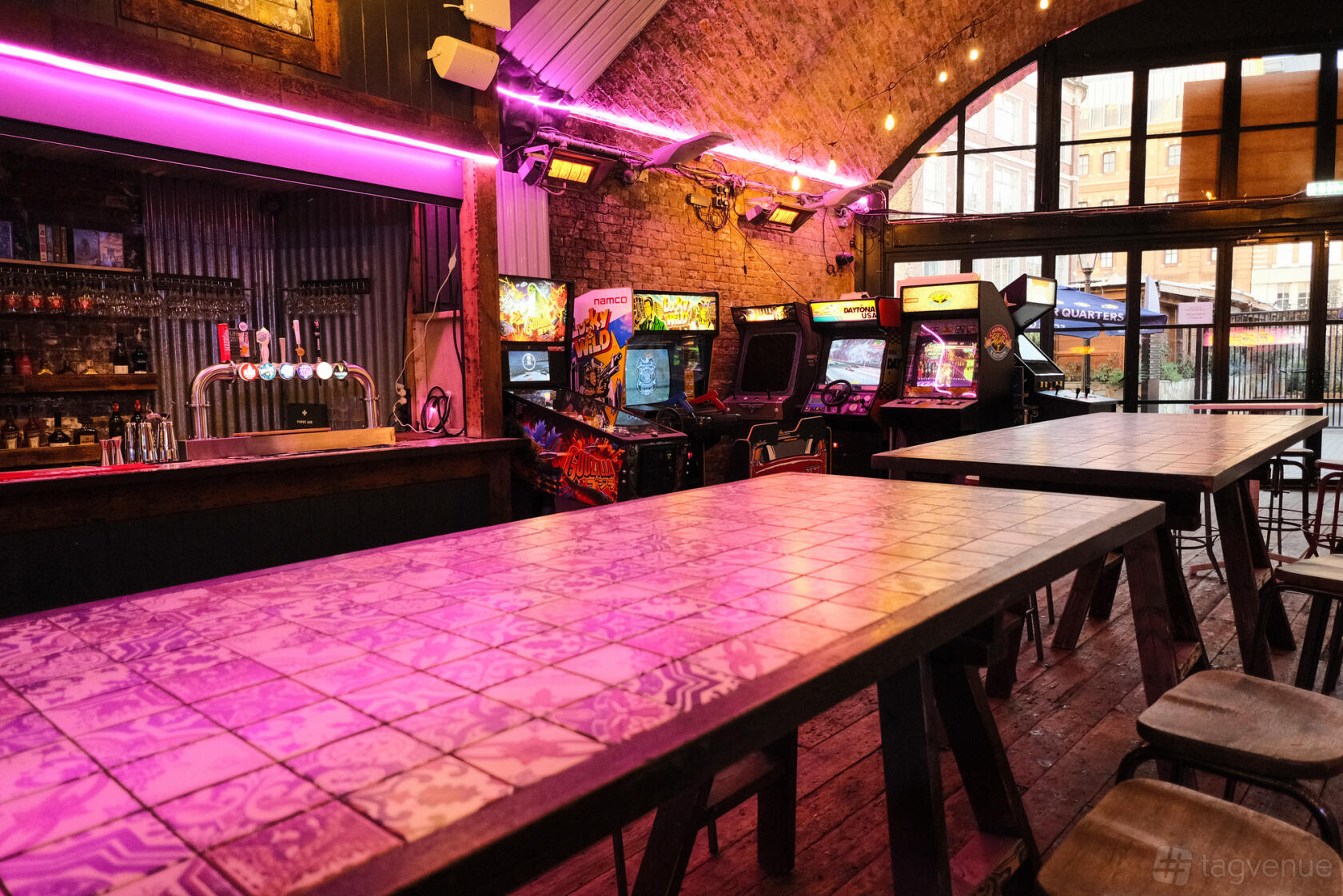 A railway arch bar with exposed brick ceiling, arcade game machines, and long tiled tables at Four Quarters.