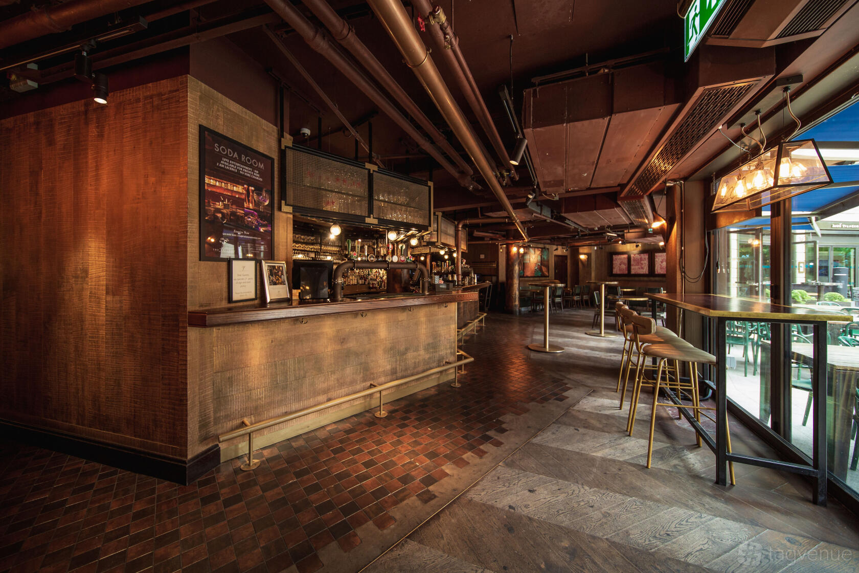 A lounge in a restaurant with an industrial-style bar, pendant lighting, and tall windows at The Botanist Broadgate Circle.
