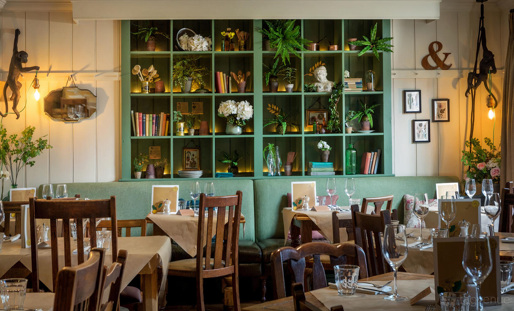 A function room in a restaurant with wooden chairs, set tables, and a green shelving unit with plants at The King's Head, Teddington.